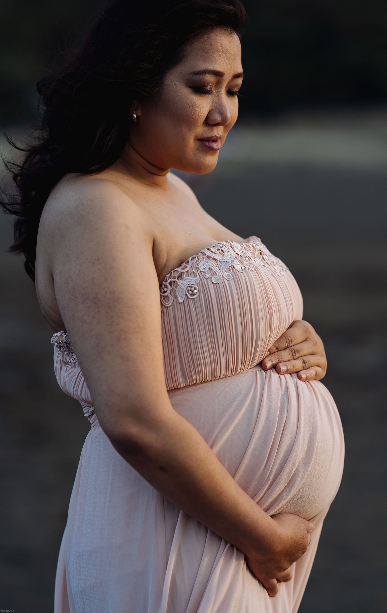 Maternity photo of an expectant mother in a blush pink strapless gown with lace details.