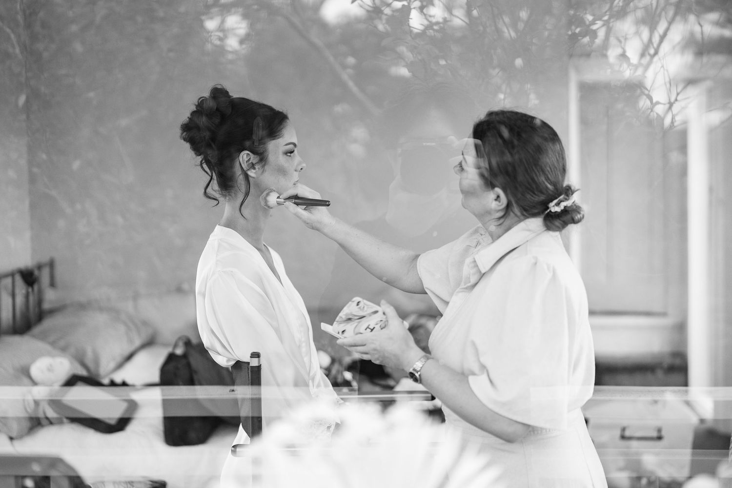 Black and white photo of wedding preparation with makeup being applied.