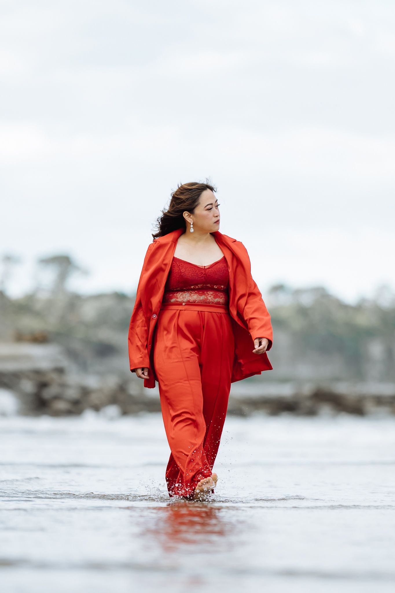 Person in flowing red dress wading through shallow ocean water during dramatic photoshoot.