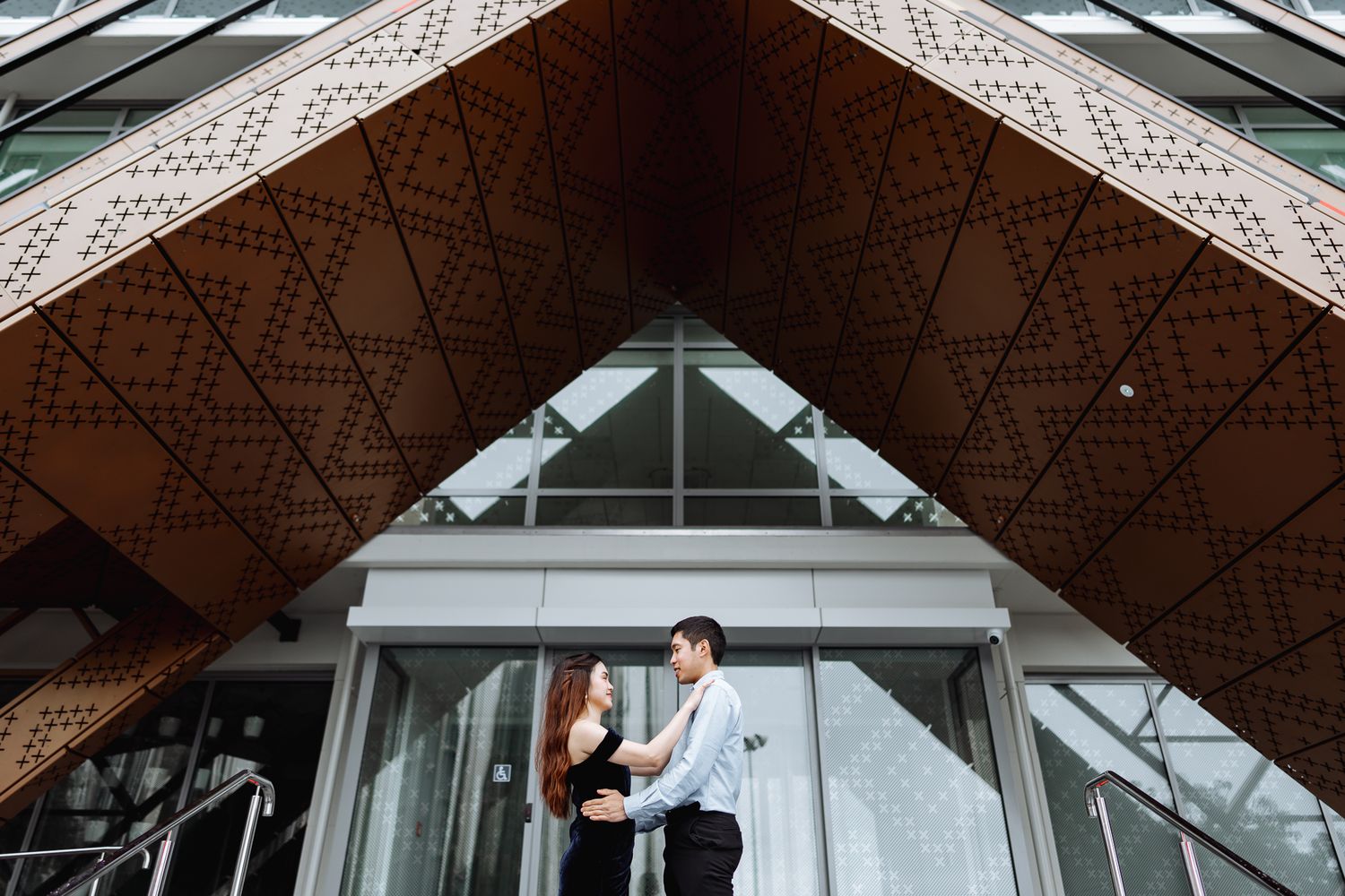 A couple poses beneath a geometric patterned architectural overhang.