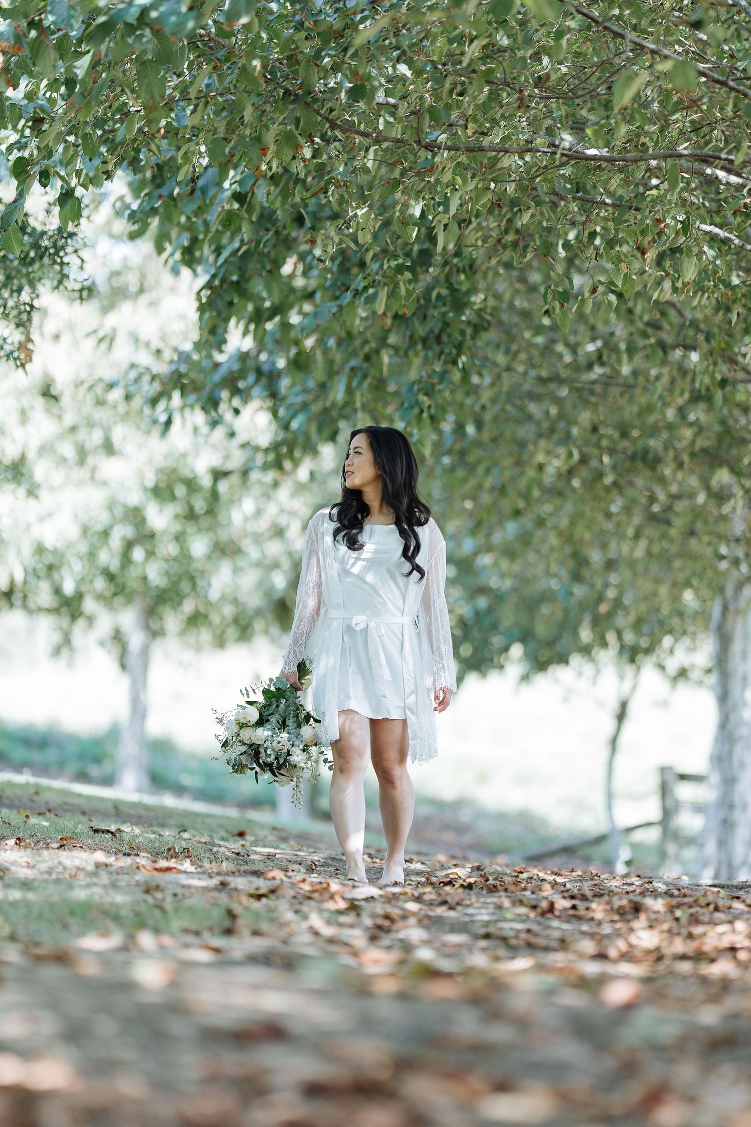 Artistic bridal portrait among green trees and fallen leaves.