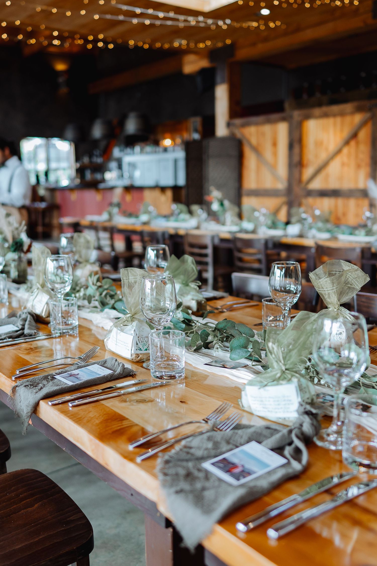Long wooden tables set for a wedding reception with elegant glassware and greenery centerpieces.