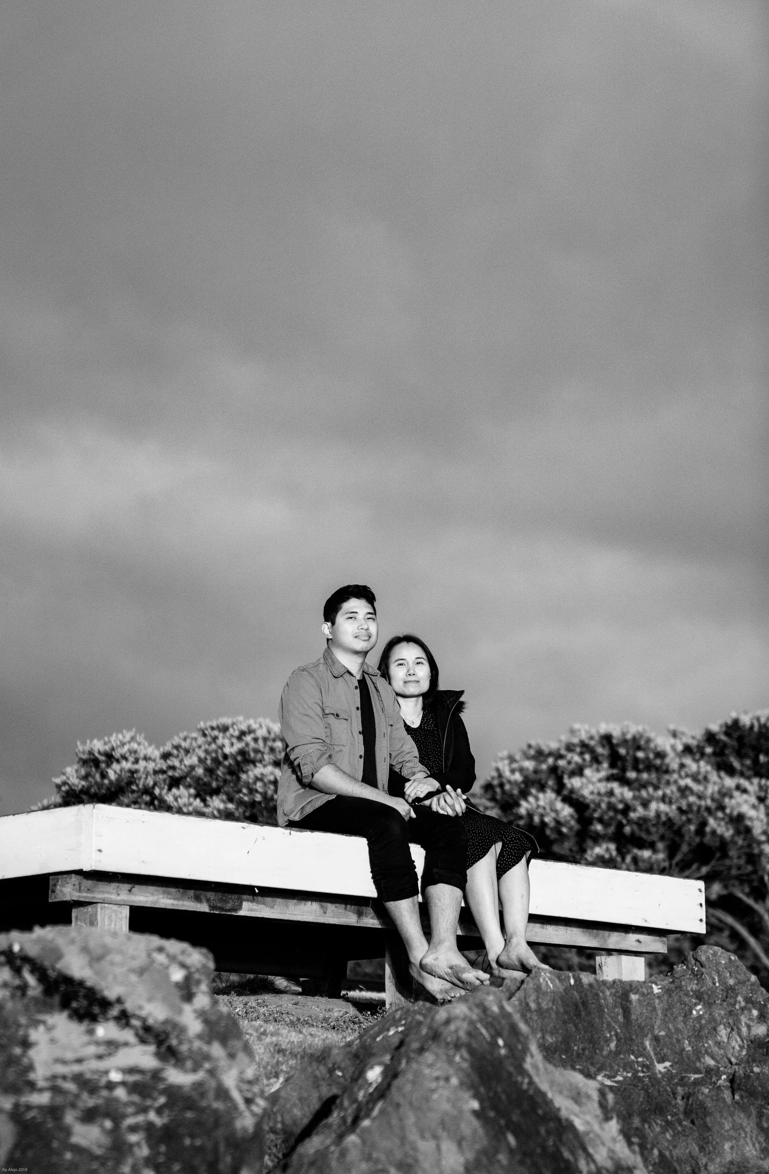 Couple relaxing together on a concrete ledge against a moody sky in black and white.