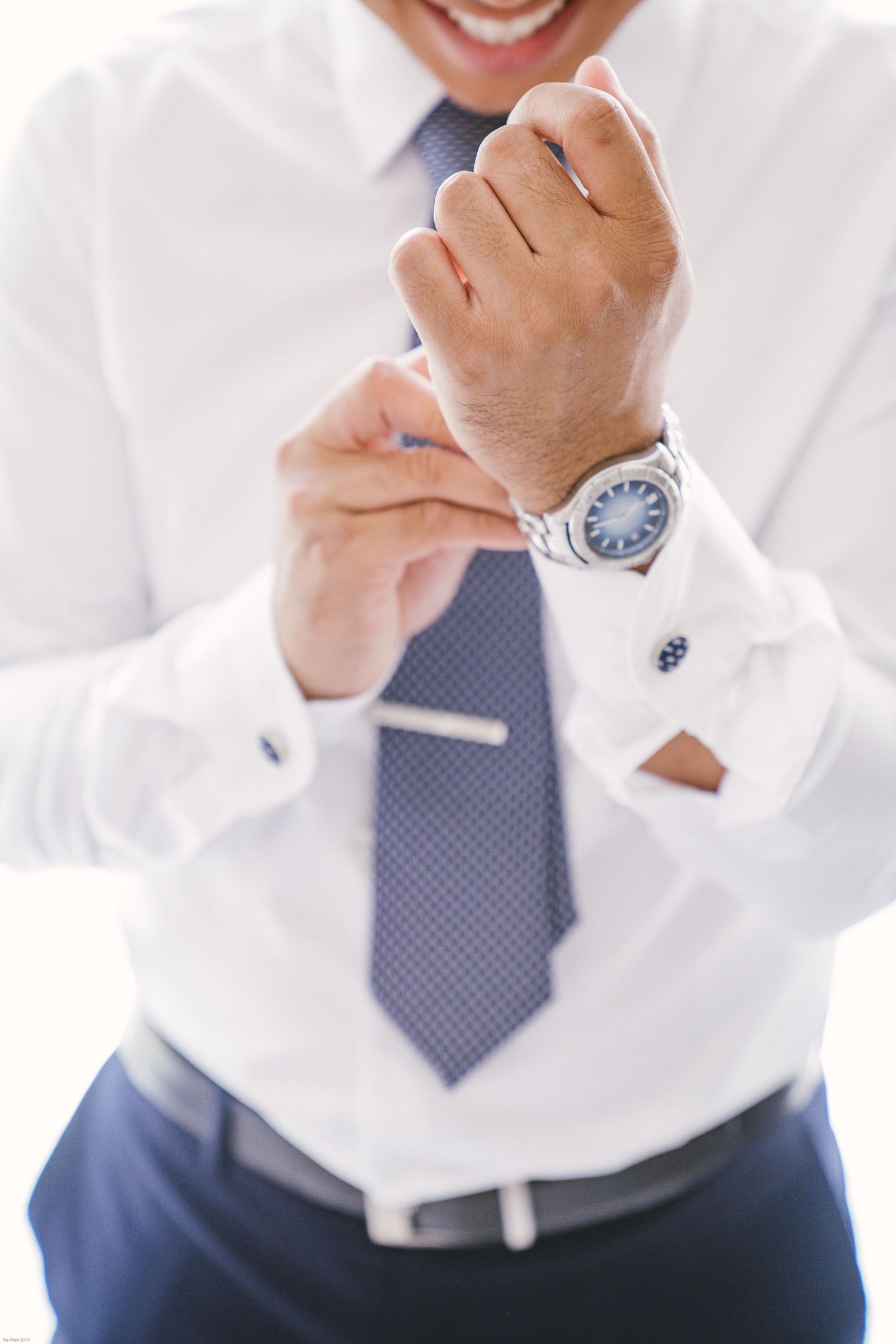 Close-up of formal attire with blue tie and watch while adjusting cufflinks.