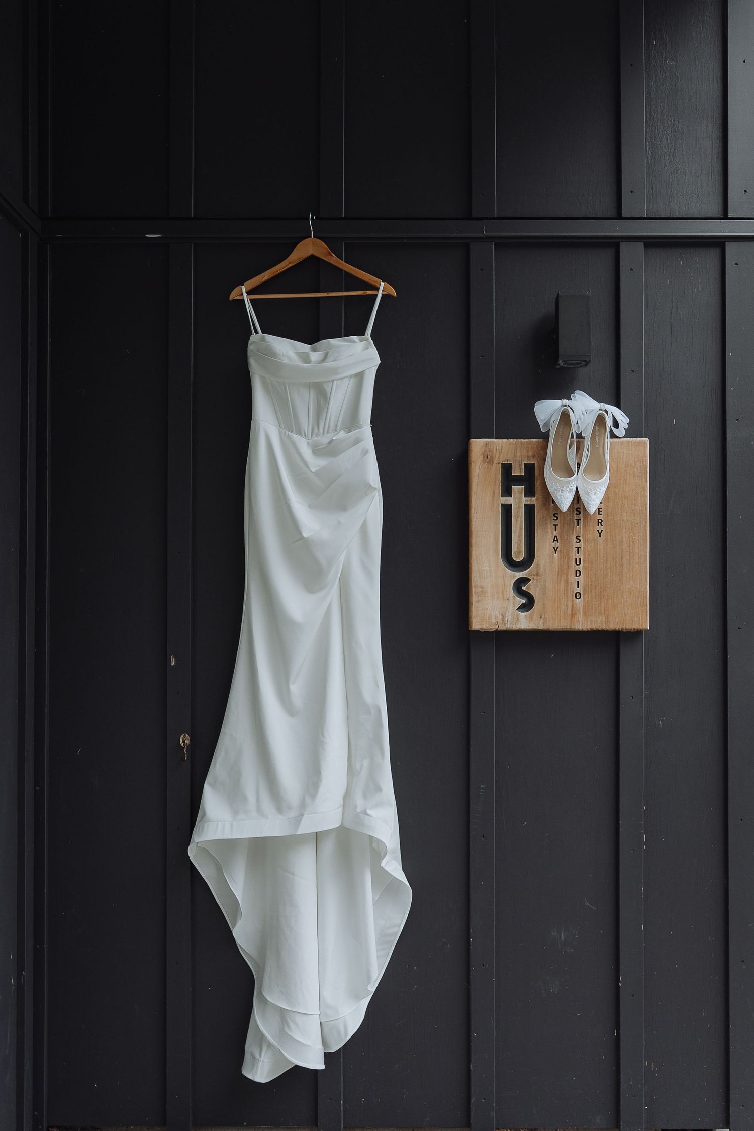 A white wedding dress hangs elegantly against a dark wall with accessories displayed.