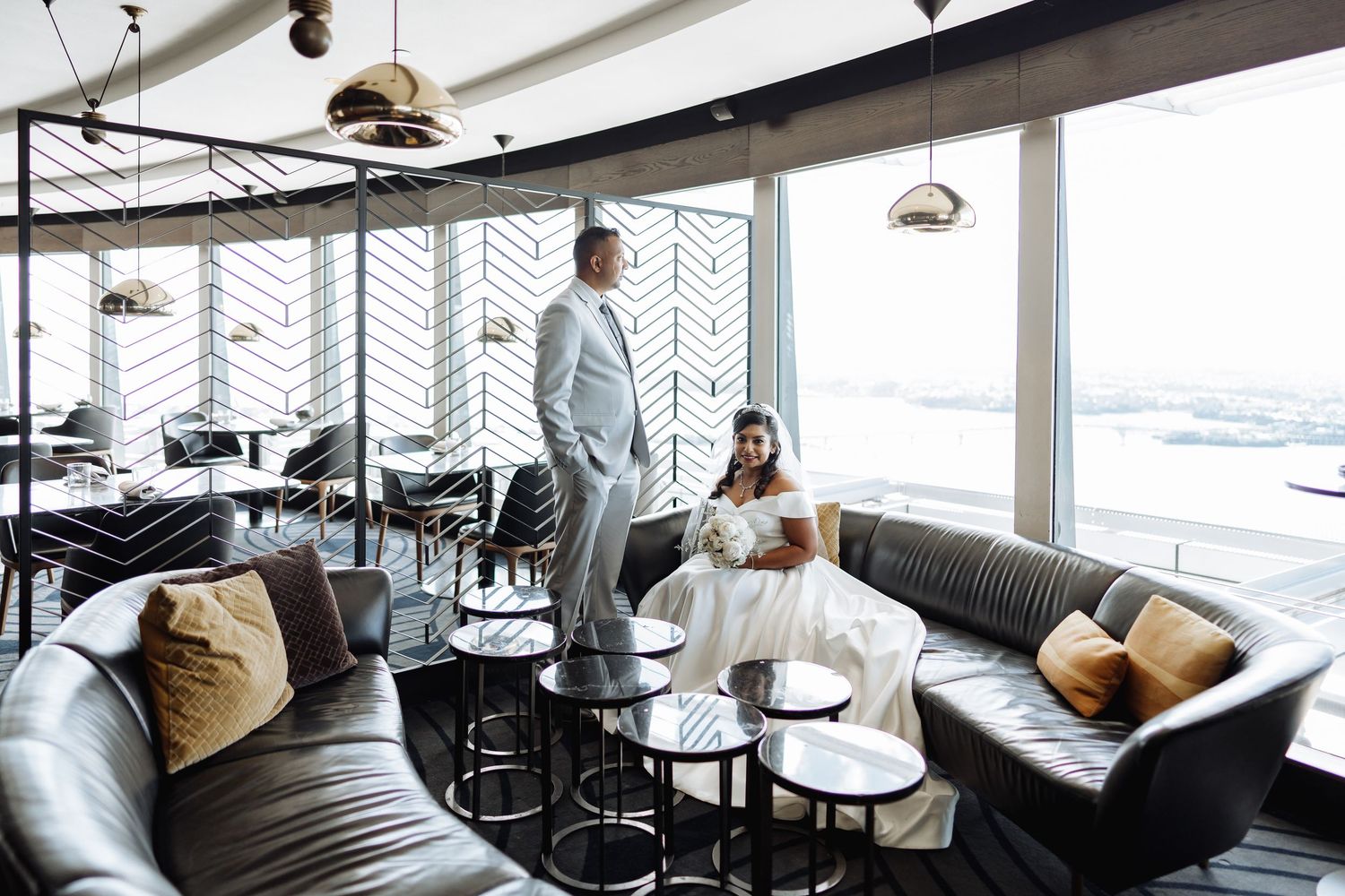 Modern restaurant wedding photo with geometric patterns and city views through large windows.