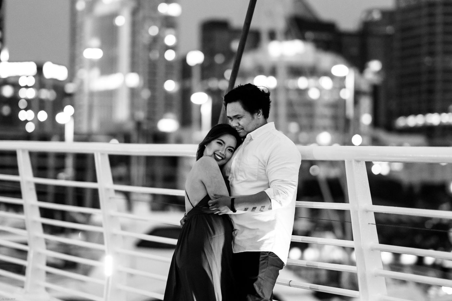Couple sharing an intimate moment along a waterfront railing at night.