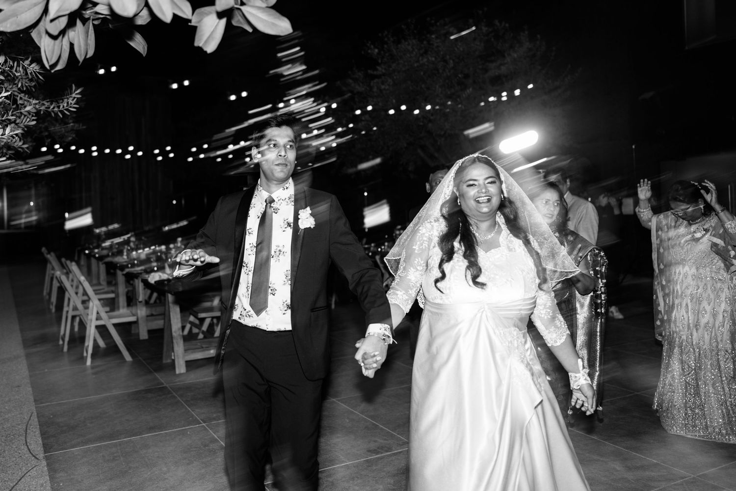Wedding celebration with dancing guests under string lights at night.