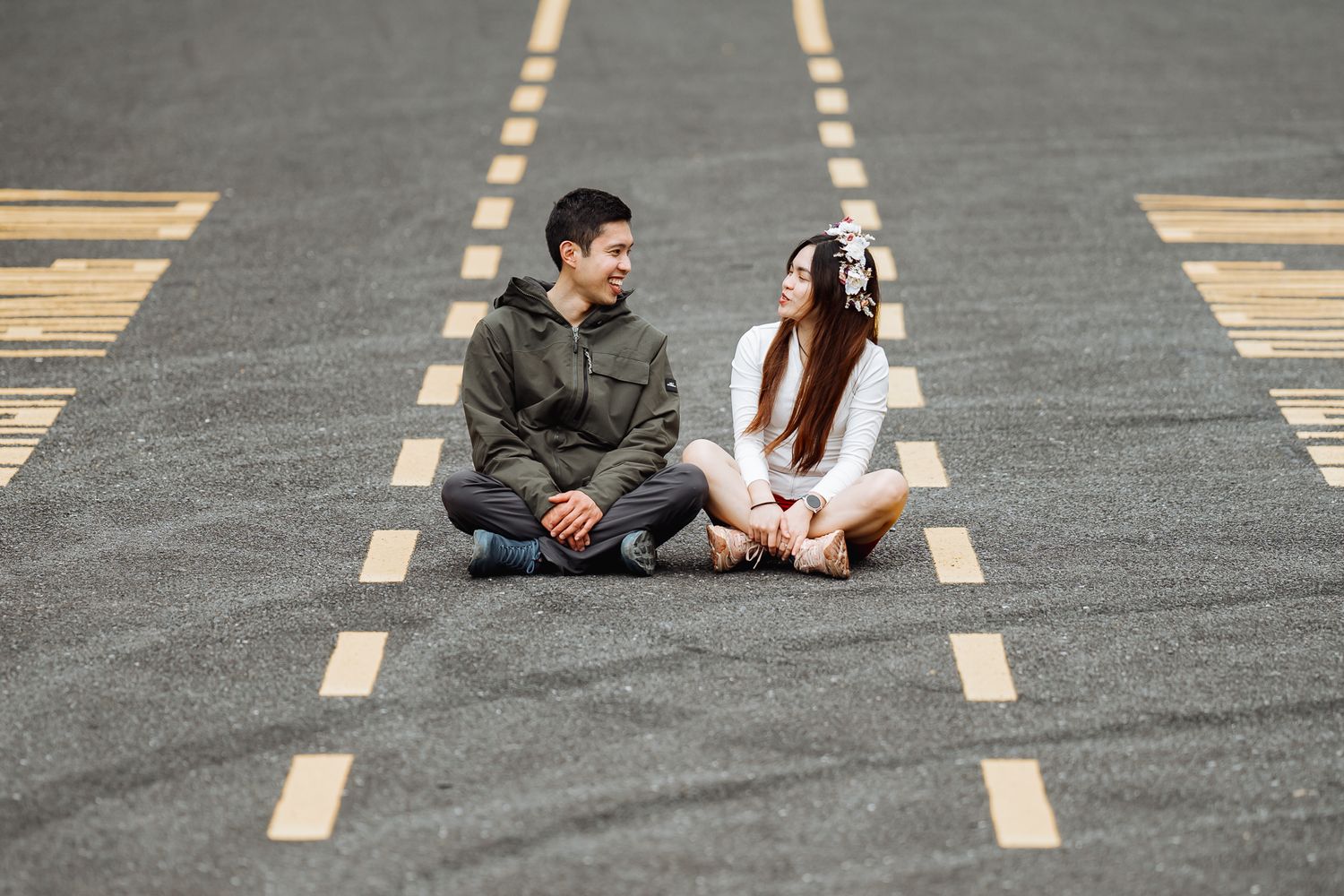Couple sitting on striped pavement in urban setting during photo session.