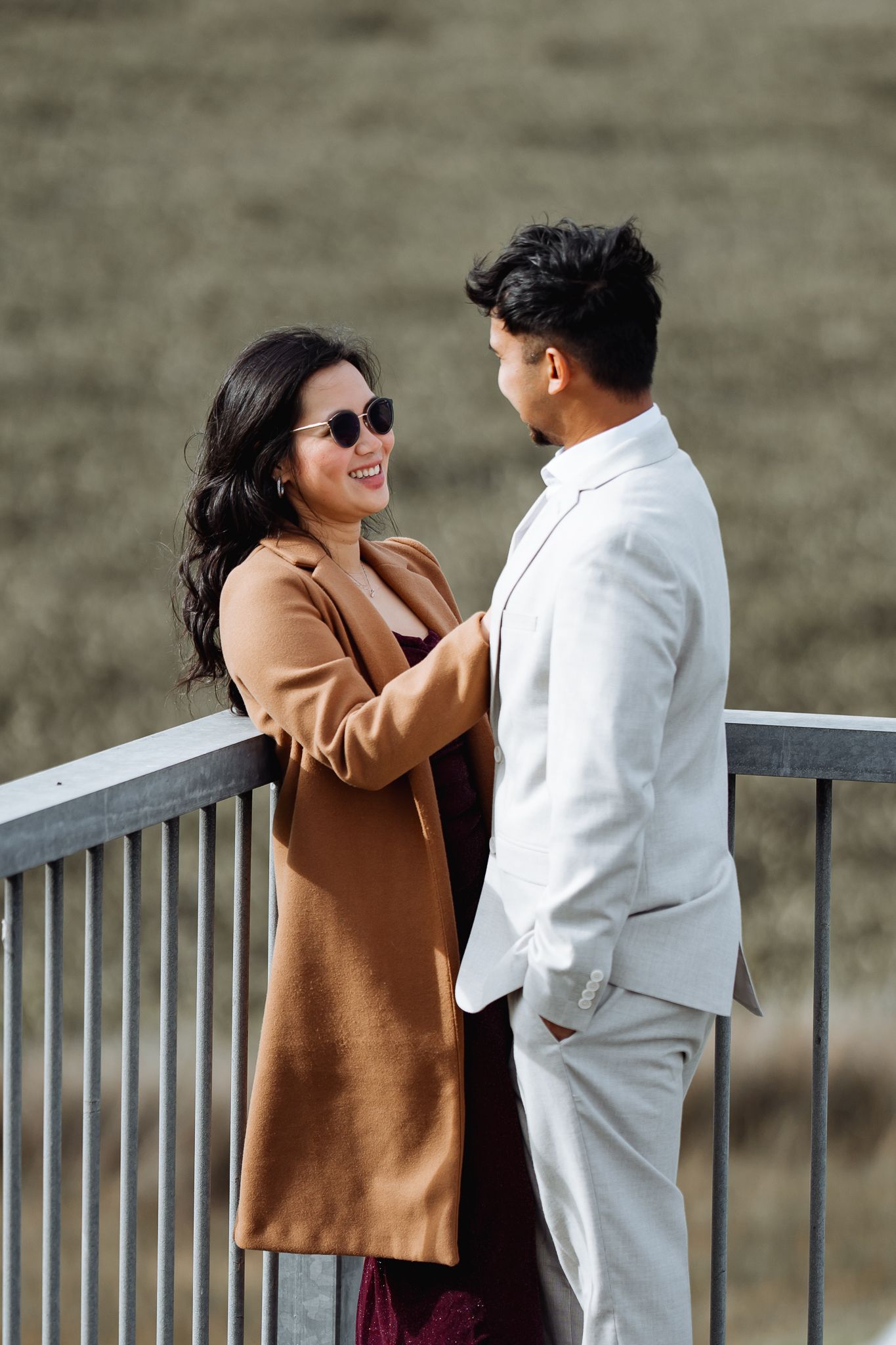 Couple in casual attire sharing playful moments by metal railings outdoors.