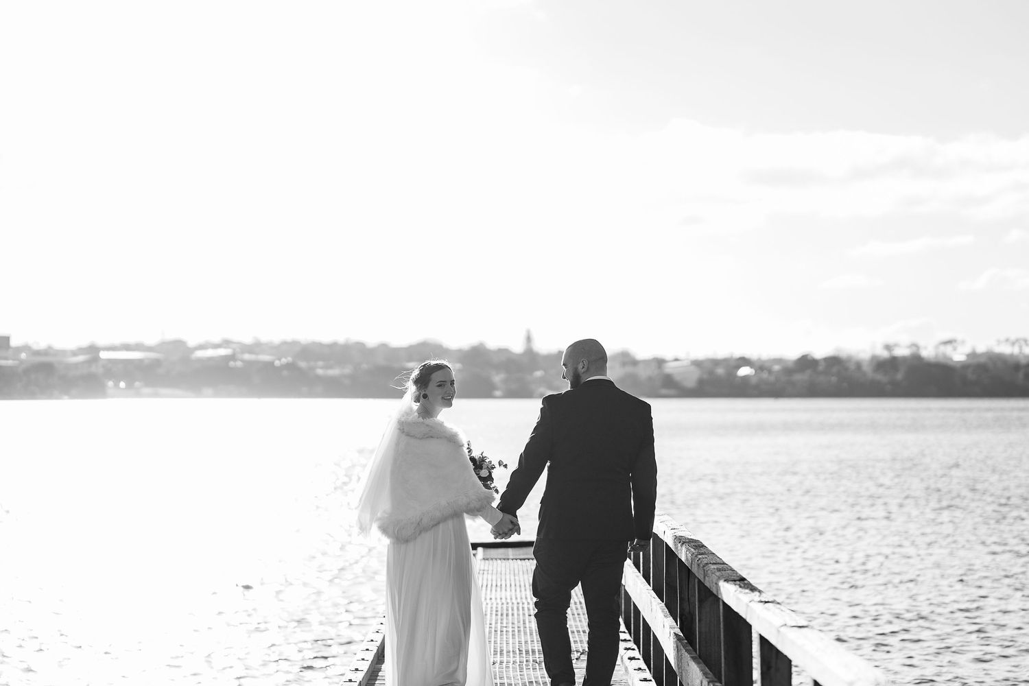 Wedding couple walking along waterfront pier at sunset.