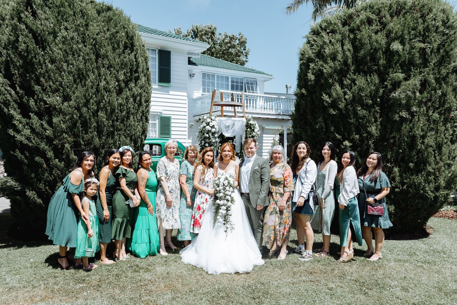 Wedding party in teal dresses poses on grass with white house in background.