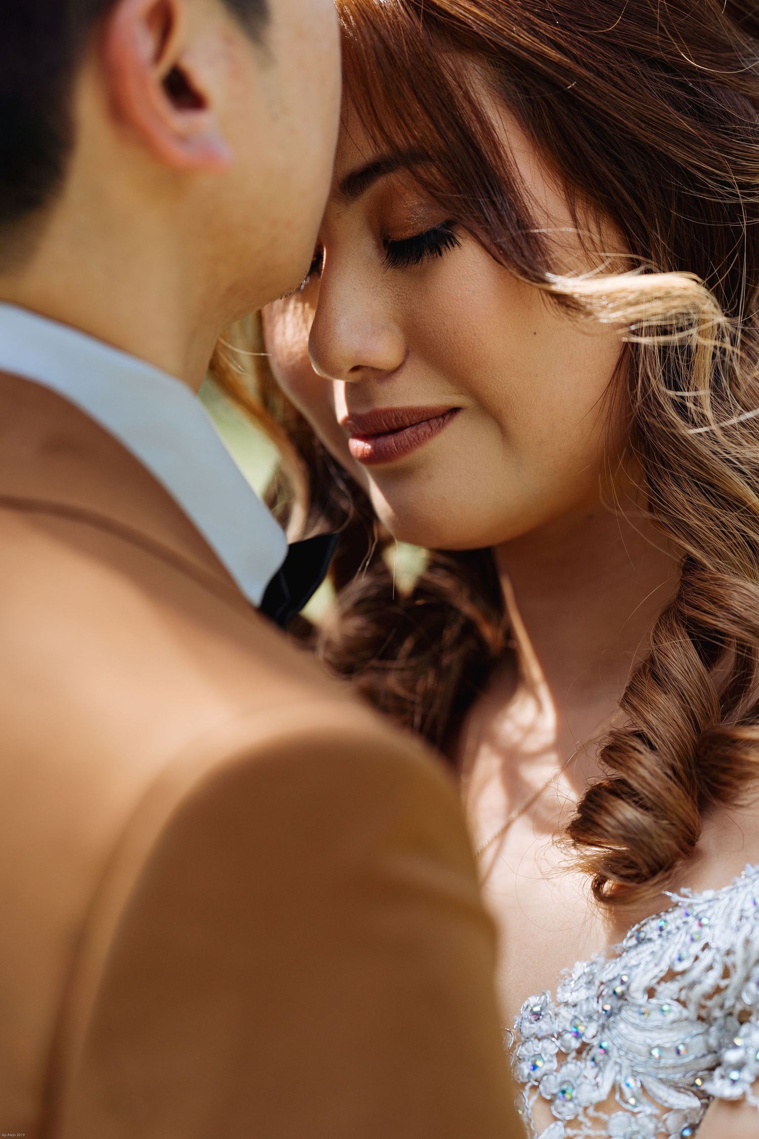 Close-up romantic moment between couple with bride wearing lace dress and groom in brown suit.