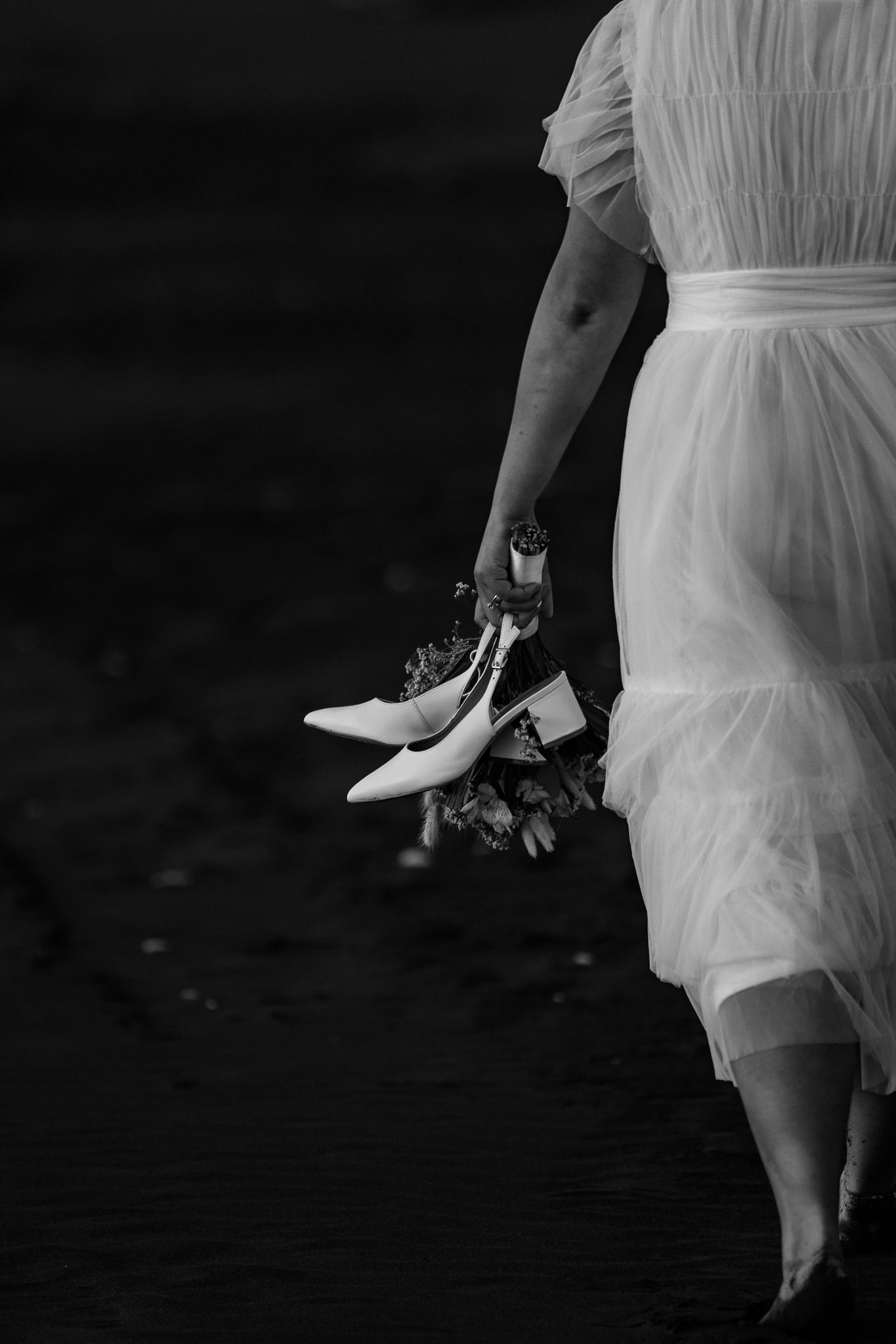 A close-up black and white photo of wedding attire details near the beach water.