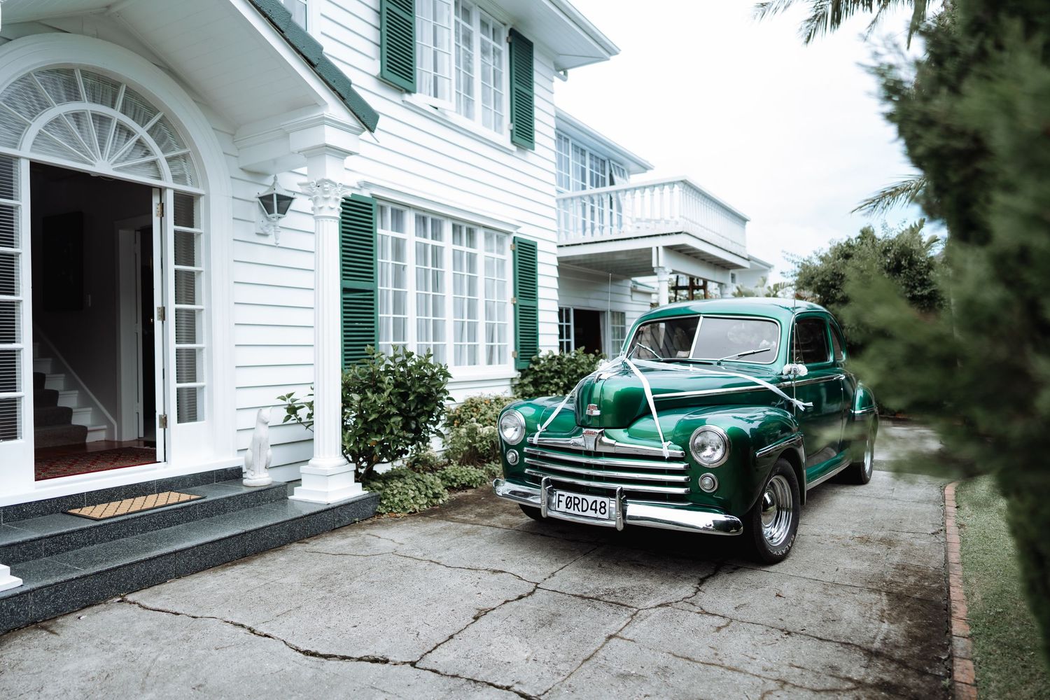 Classic white colonial style house exterior with vintage green car parked in driveway.