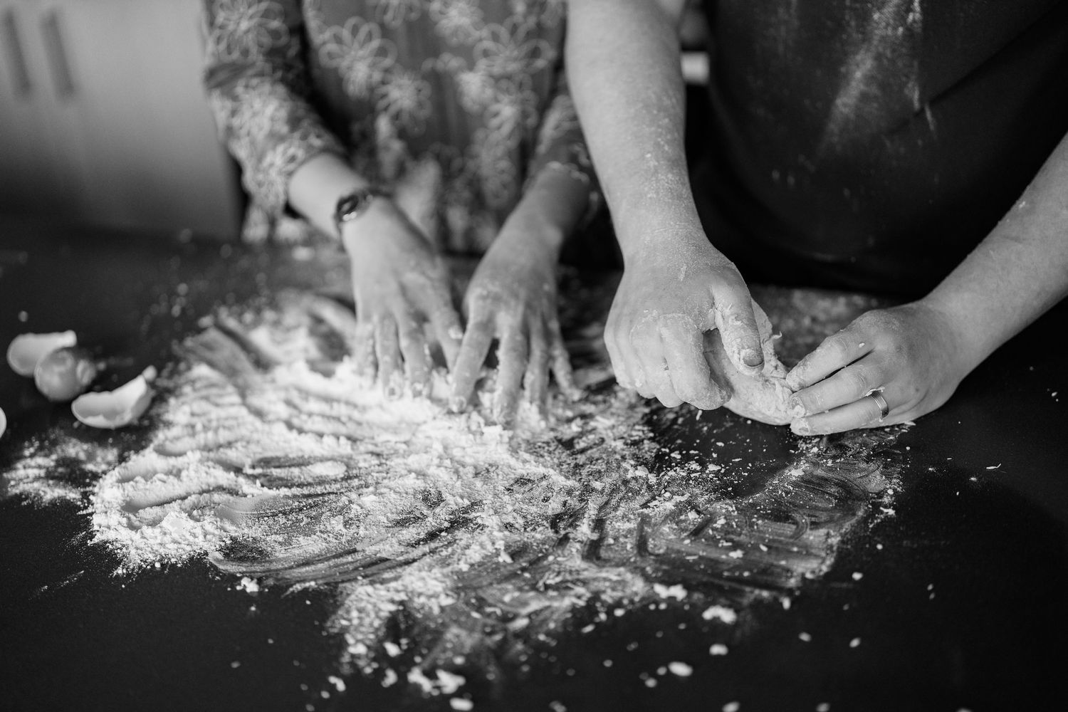 Hands kneading dough on a floured surface in black and white.