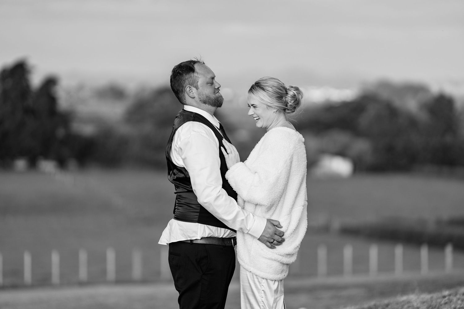 A couple in formal attire shares an intimate moment in a black and white outdoor setting.