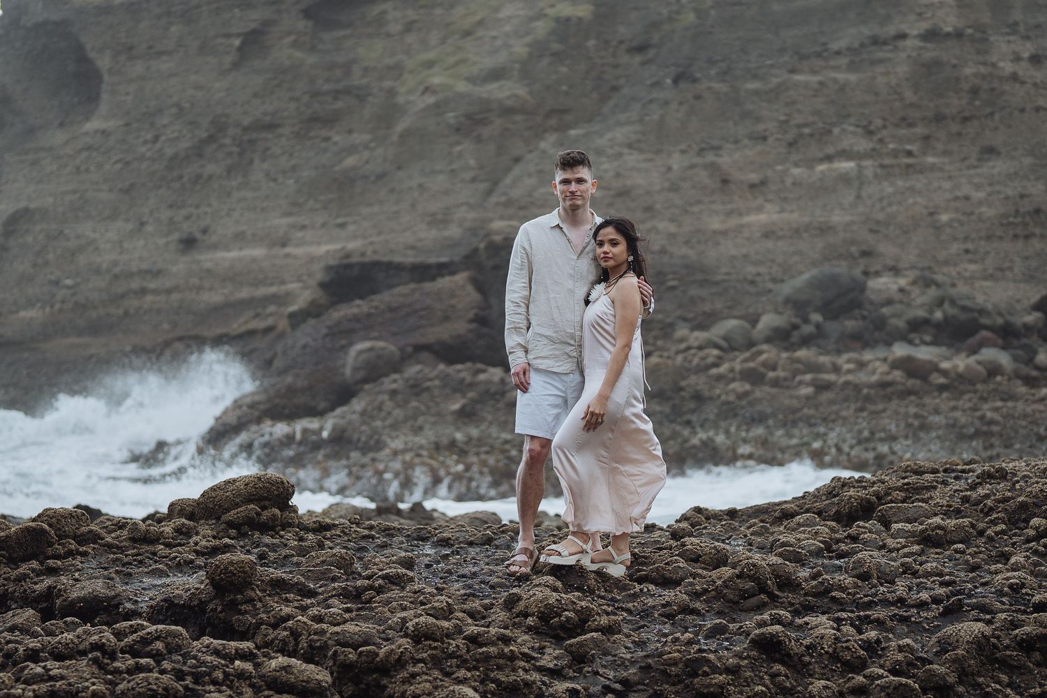 Couple in white outfits walking along dramatic coastal cliffs during sunset.