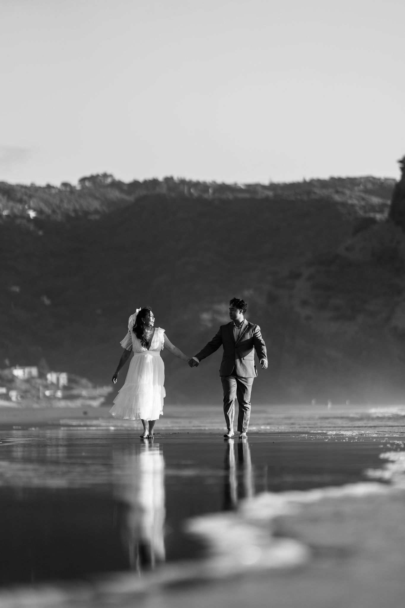 A black and white photo of a couple walking together on a misty beach.