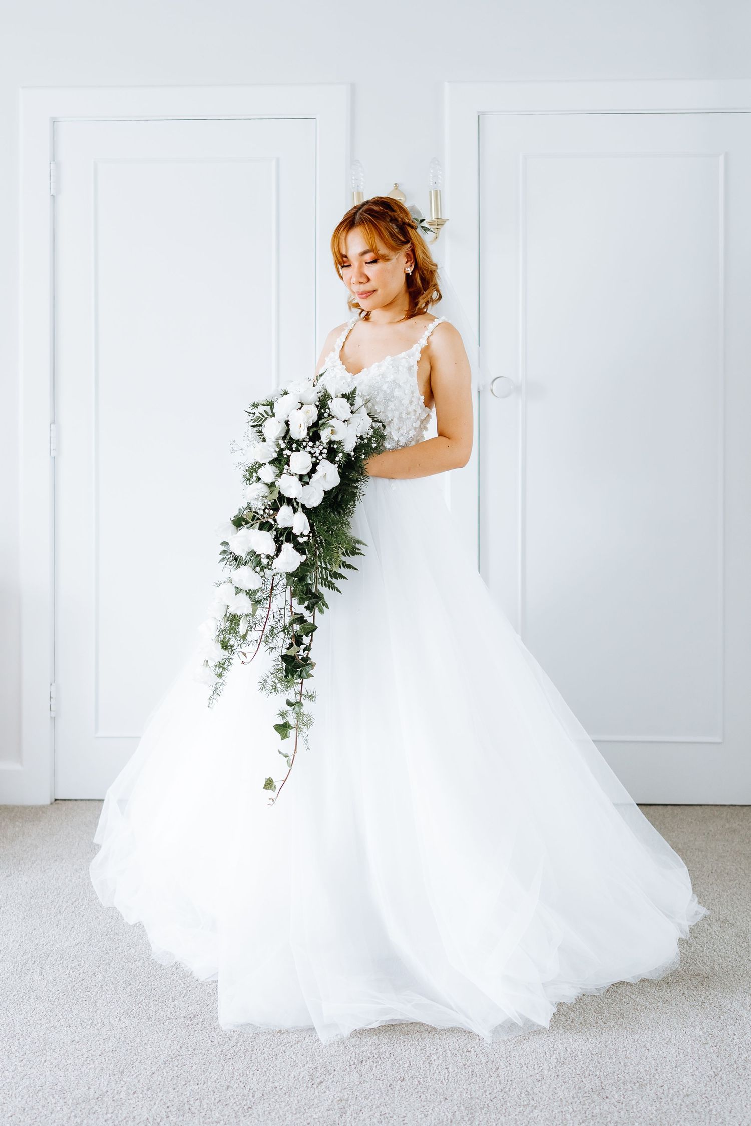 Elegant bride in a flowing white ballgown poses against white doors in a bright indoor setting.