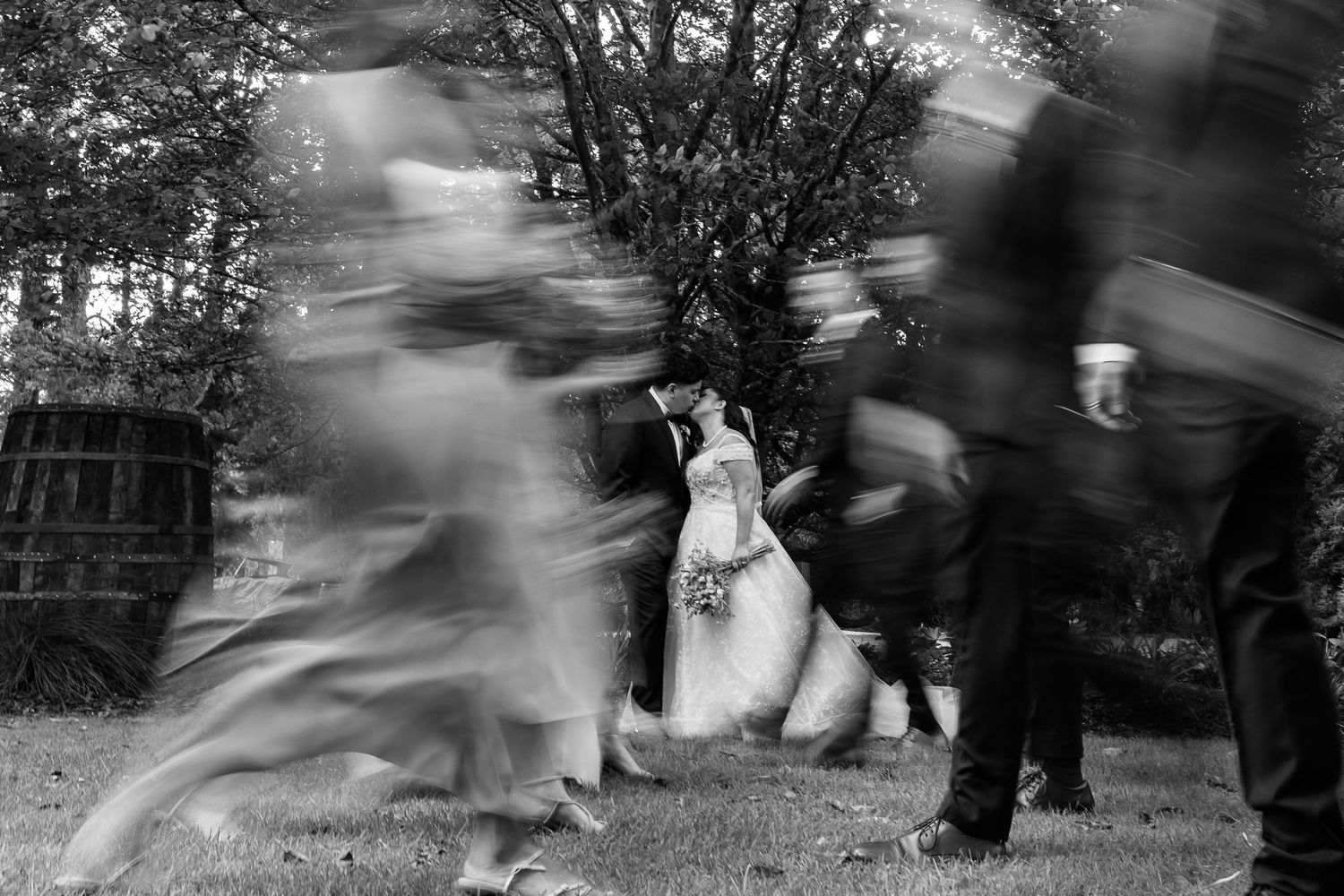 Motion-blurred black and white photo of wedding guests dancing outdoors.