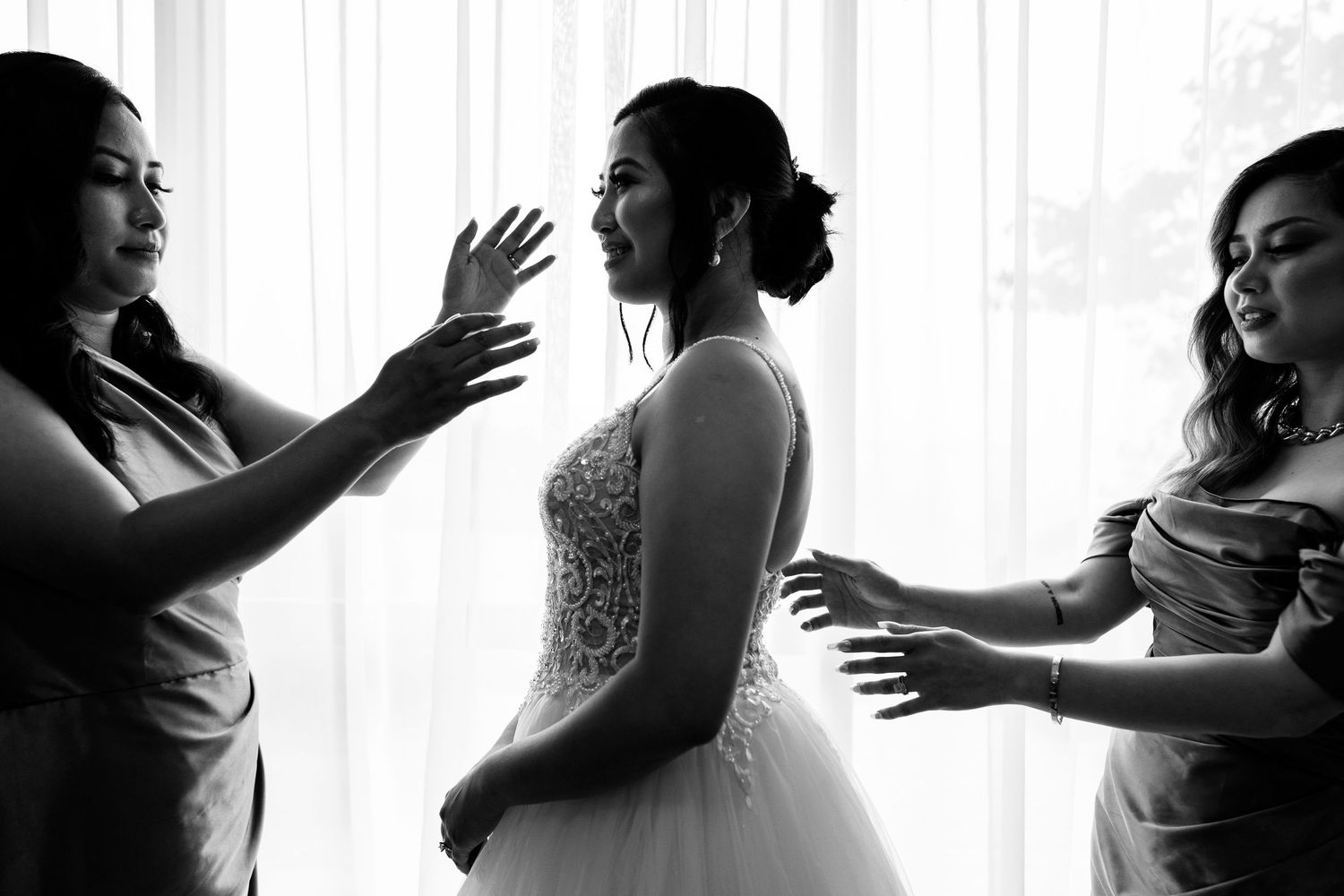 Silhouetted figures in wedding attire against bright window backlight.