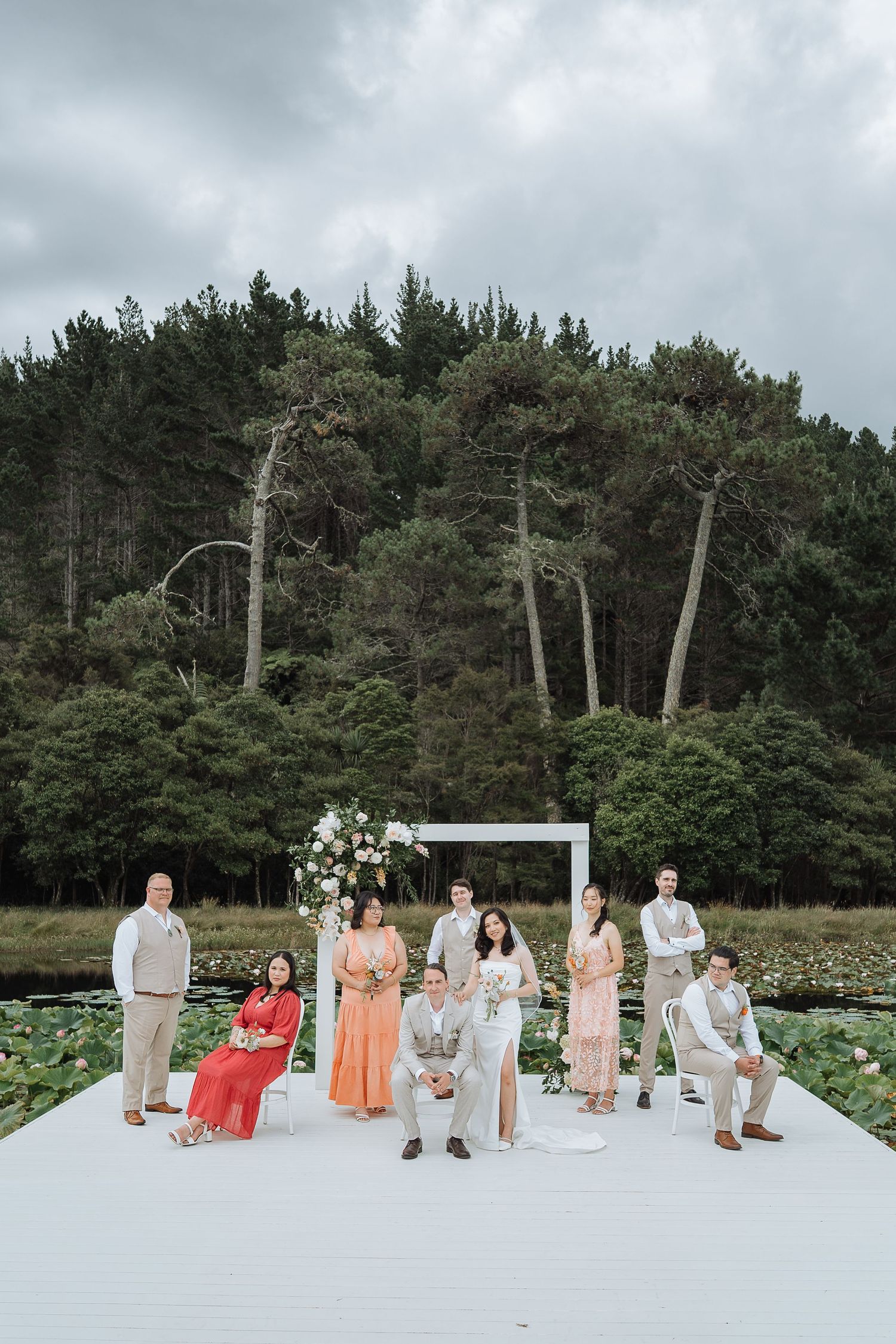 Wedding ceremony setup with white platform and floral arrangements against a backdrop of pine trees.