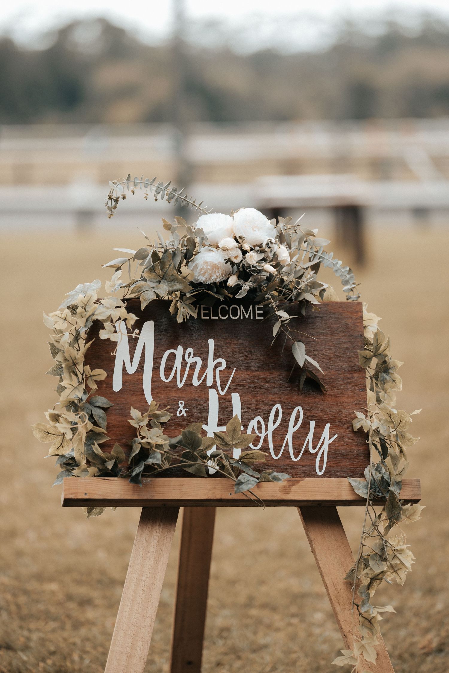 Rustic wooden wedding welcome sign decorated with white flowers and greenery.