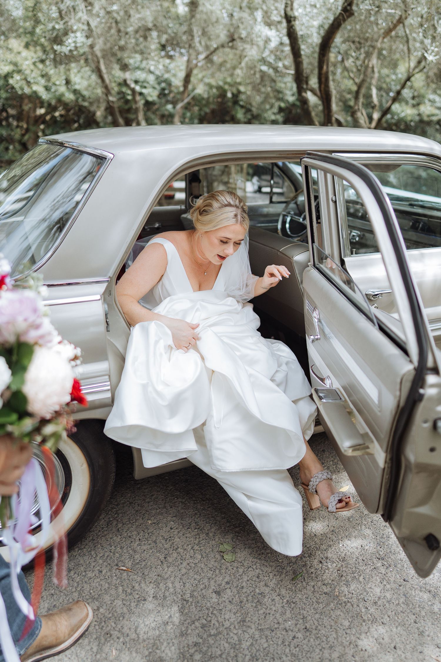 A joyful moment as someone in a white wedding dress exits a classic vintage car.