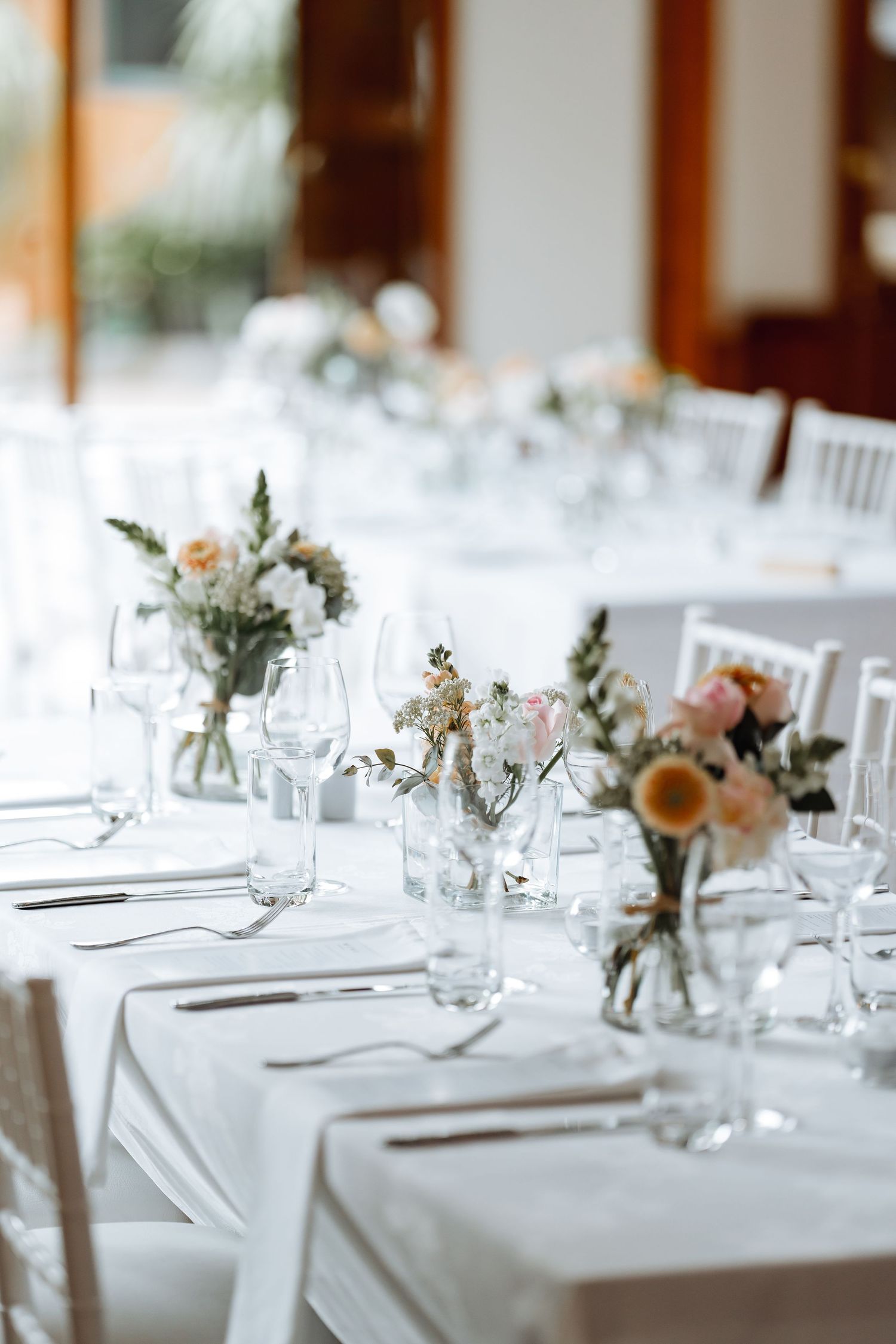 Elegant wedding reception tables set with white linens and delicate floral centerpieces in glass vases.