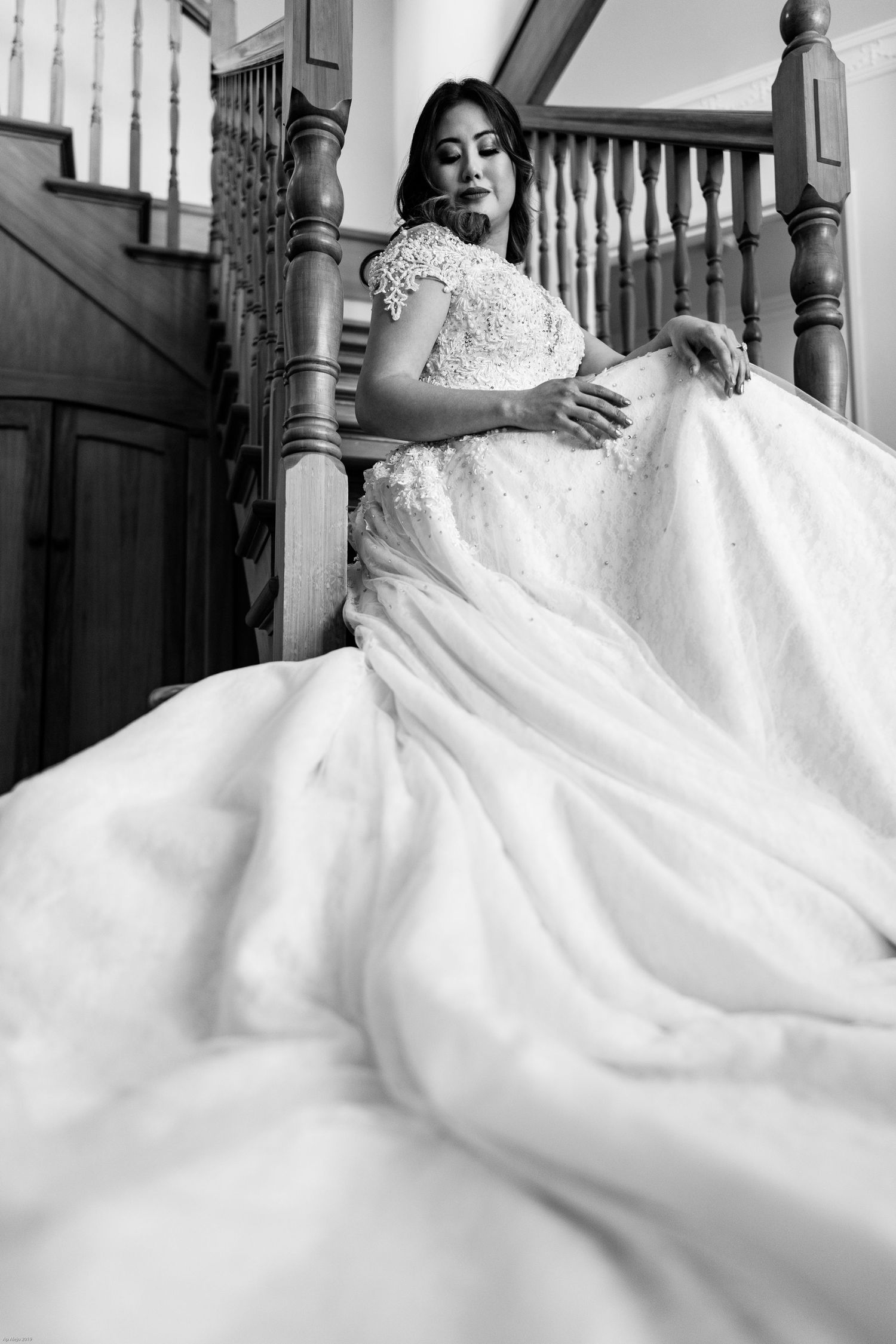 A flowing white wedding gown cascades down wooden stairs in an elegant composition.