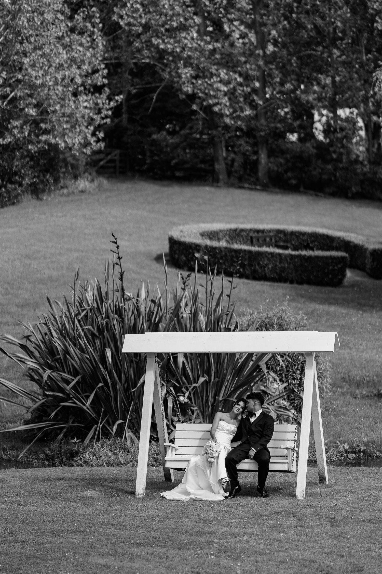 Black and white photo of couple sitting on white bench surrounded by garden landscaping.