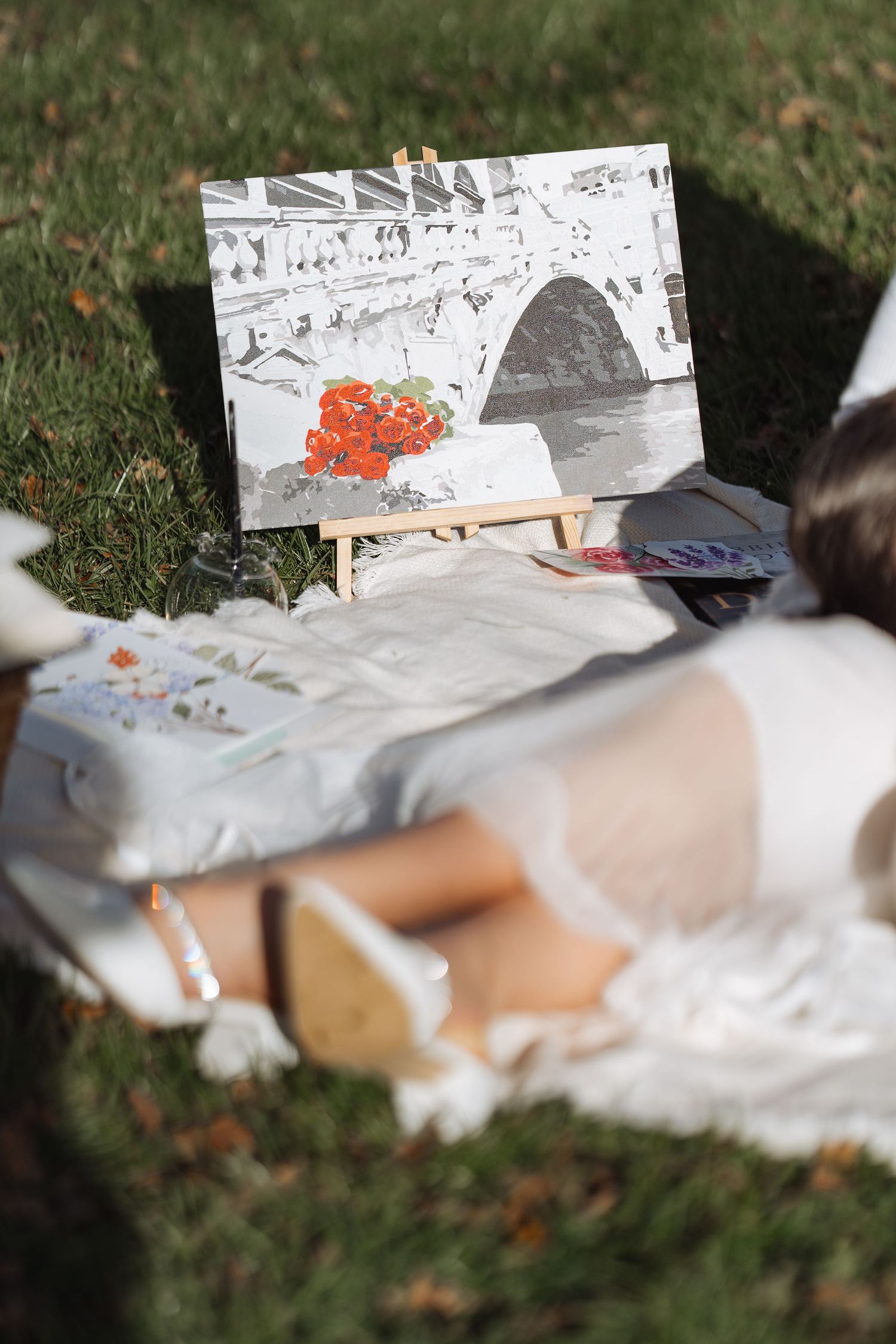 A white dress spreads across green grass next to artistic sketches and drawings.