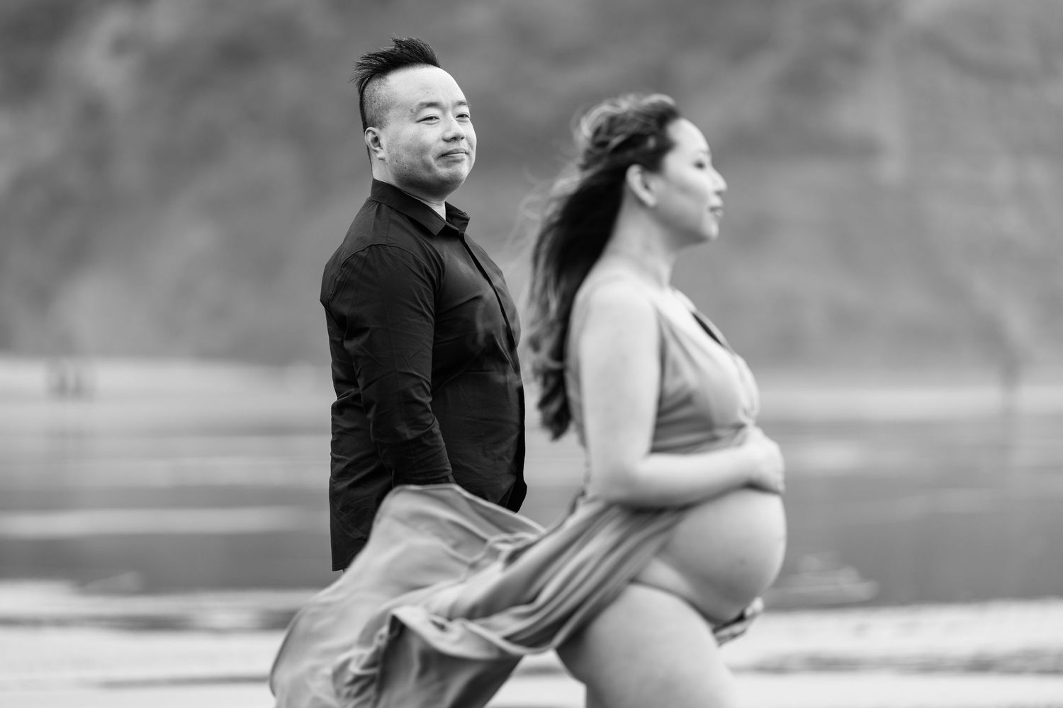 A couple shares a playful moment on the beach with dramatic cliffs in the background.