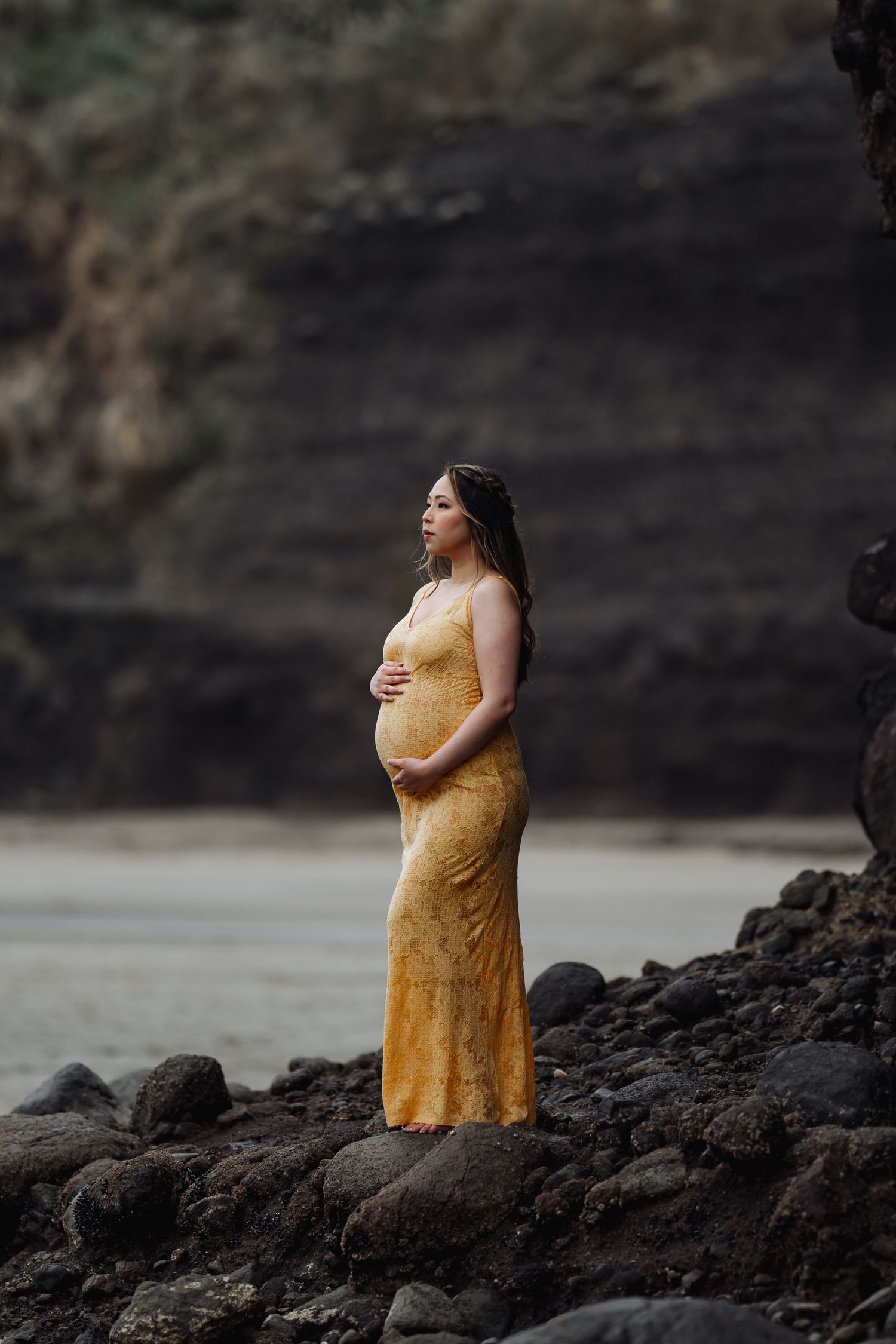 Person in yellow dress standing on rocky coastal terrain at sunset.