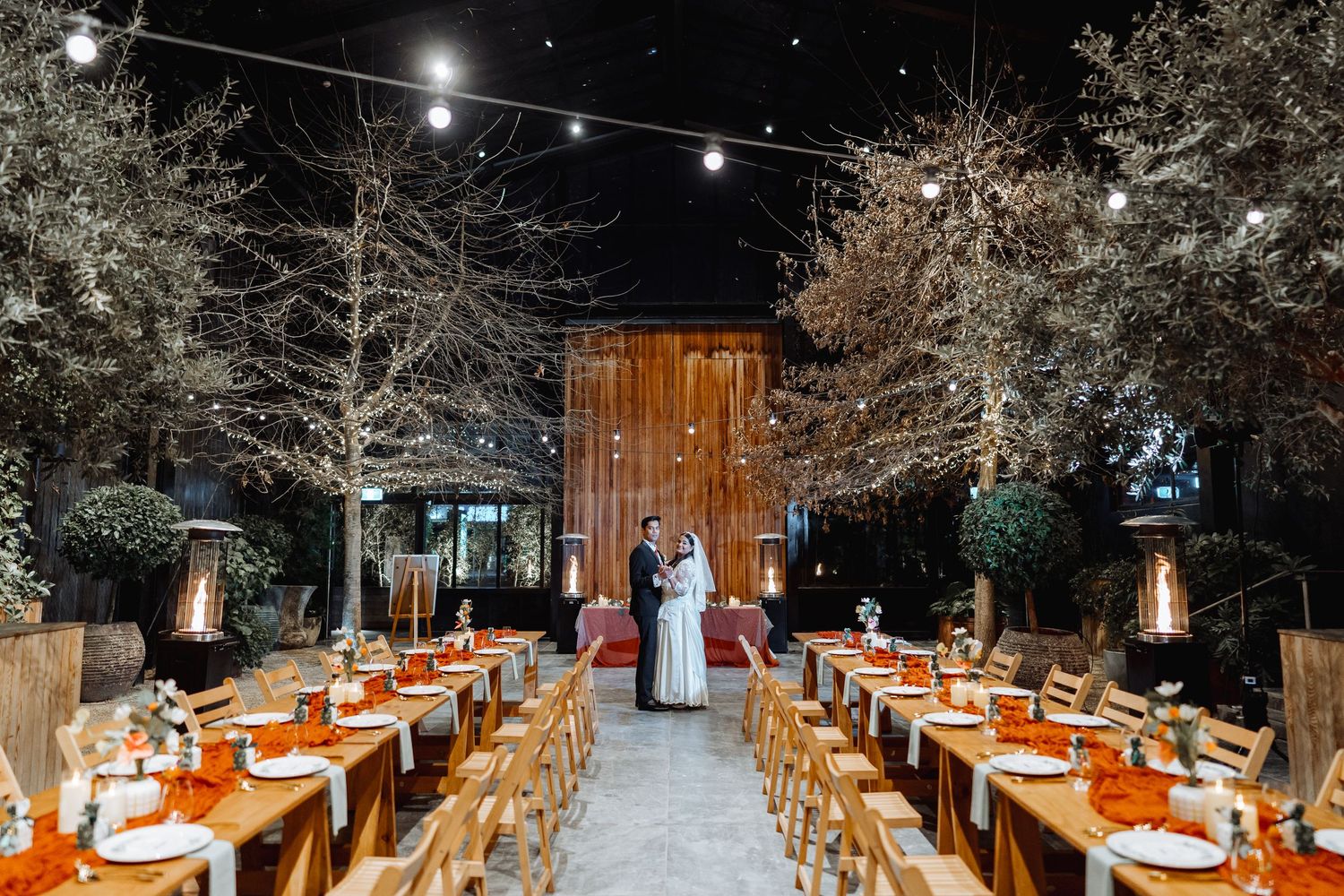 An elegant outdoor wedding reception setup with string lights and rustic wooden tables.