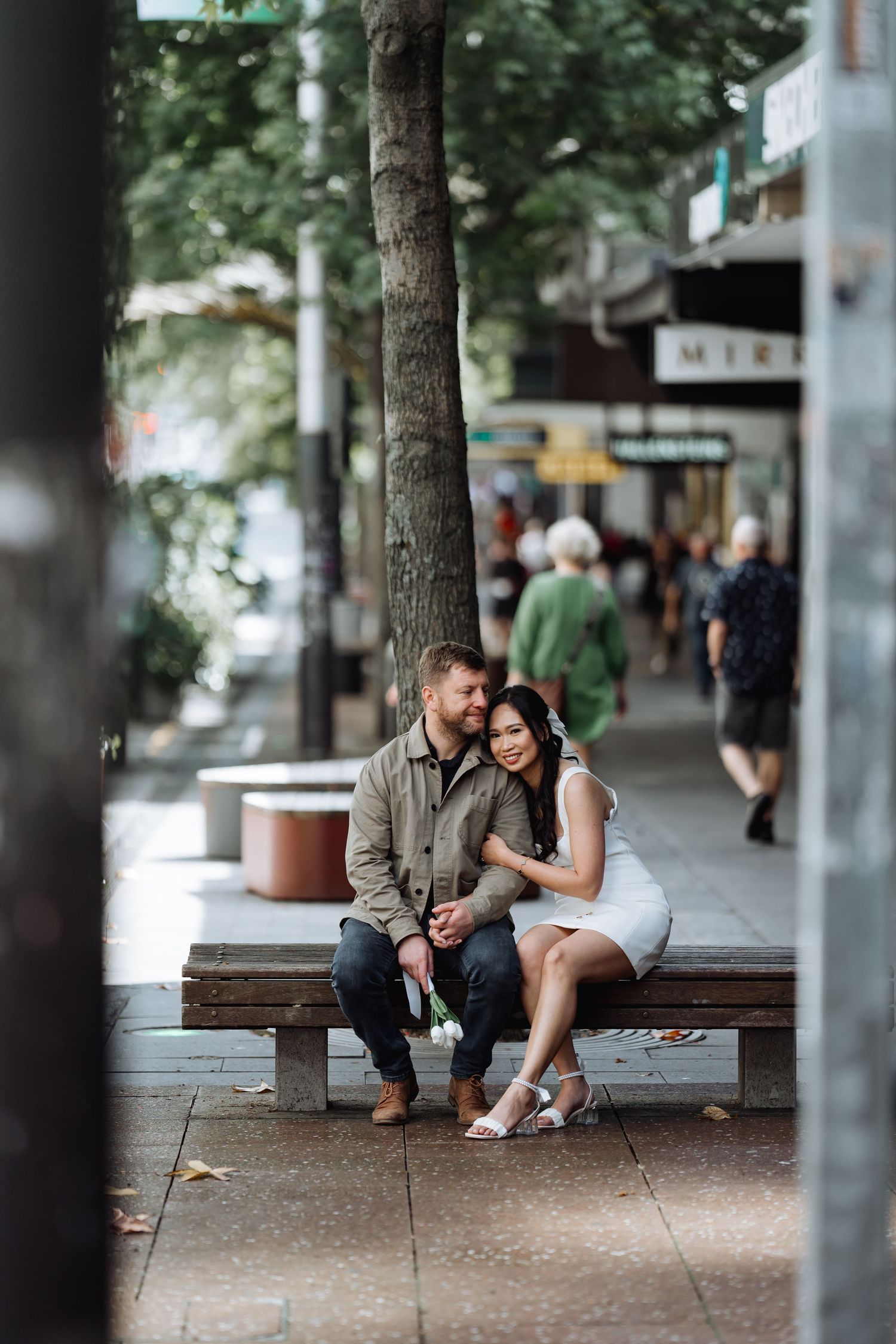 Couple sitting close together on urban street bench surrounded by trees.