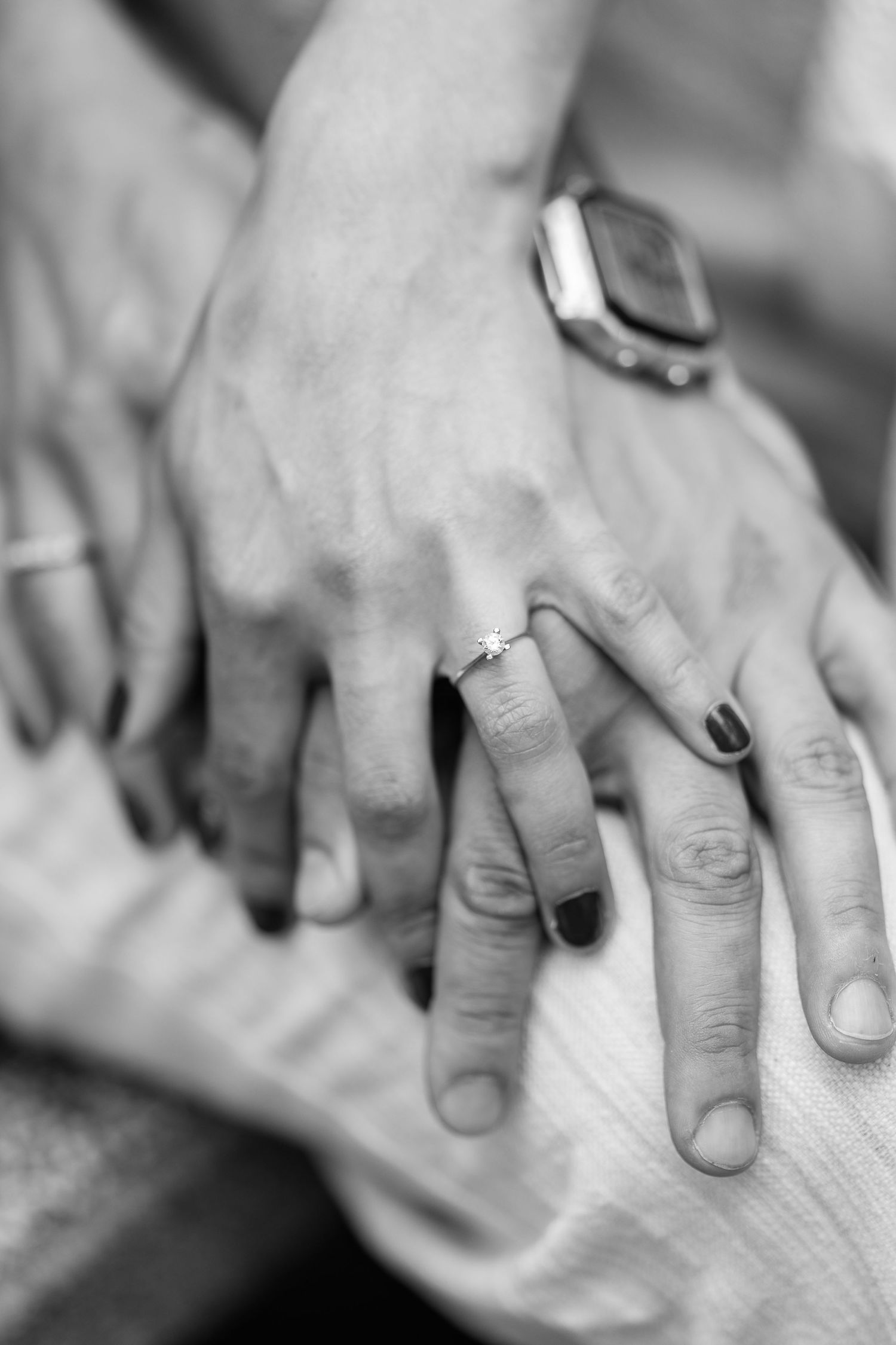 Close-up black and white photo of hands with wedding rings touching.