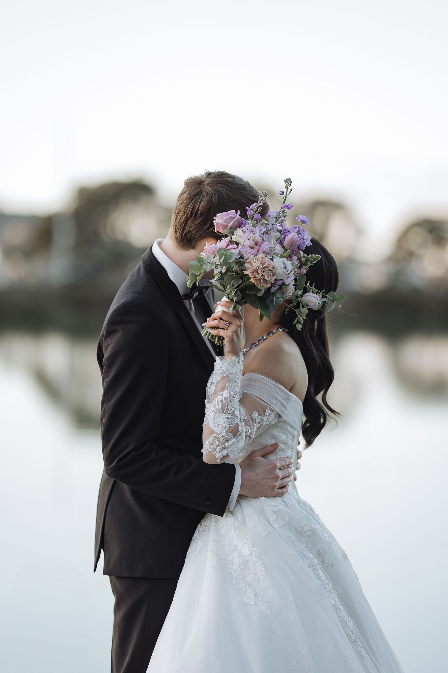 Romantic waterfront wedding portraits with soft pastel floral accents.