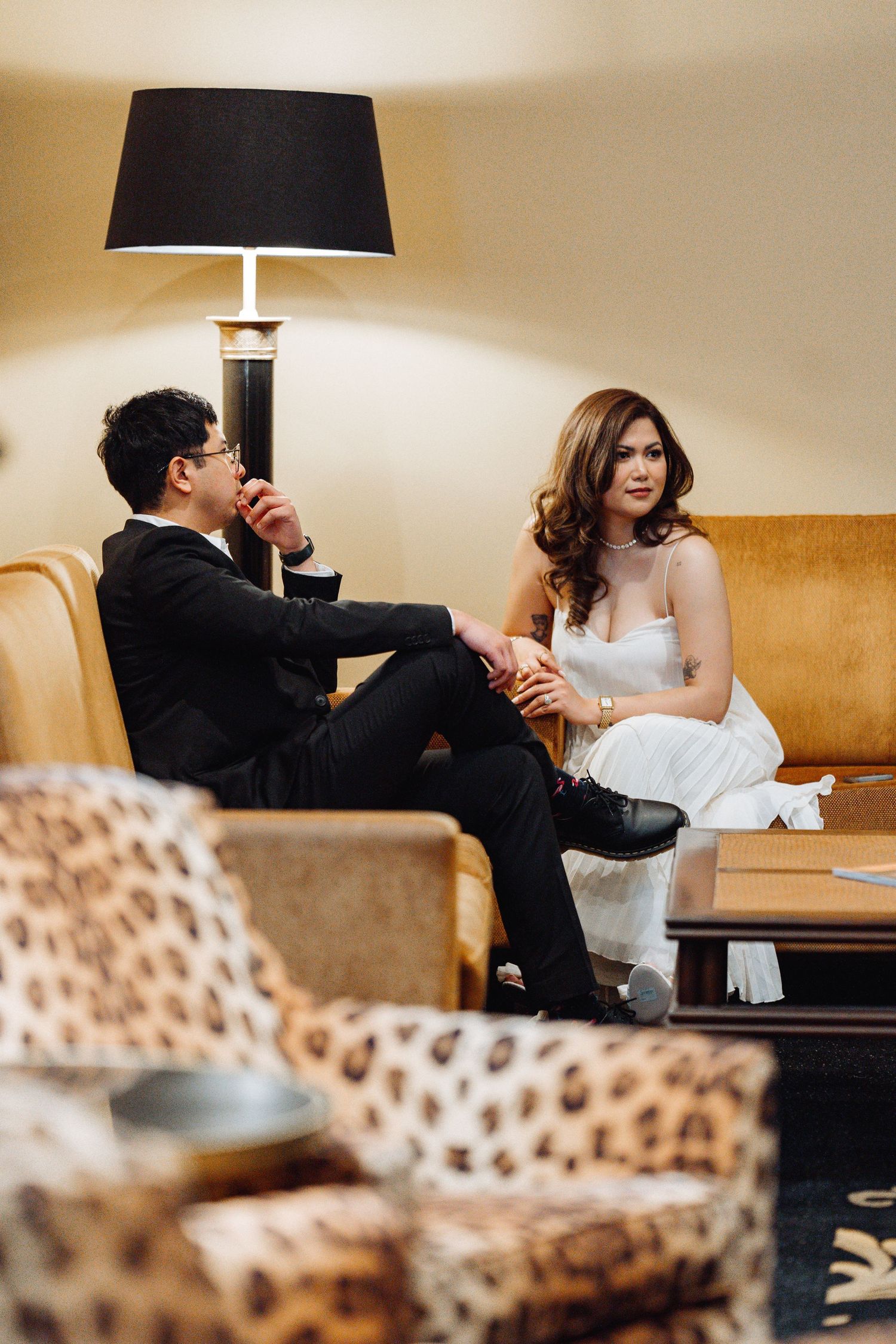 A couple relaxes on a tan leather couch with leopard print chairs and modern decor.