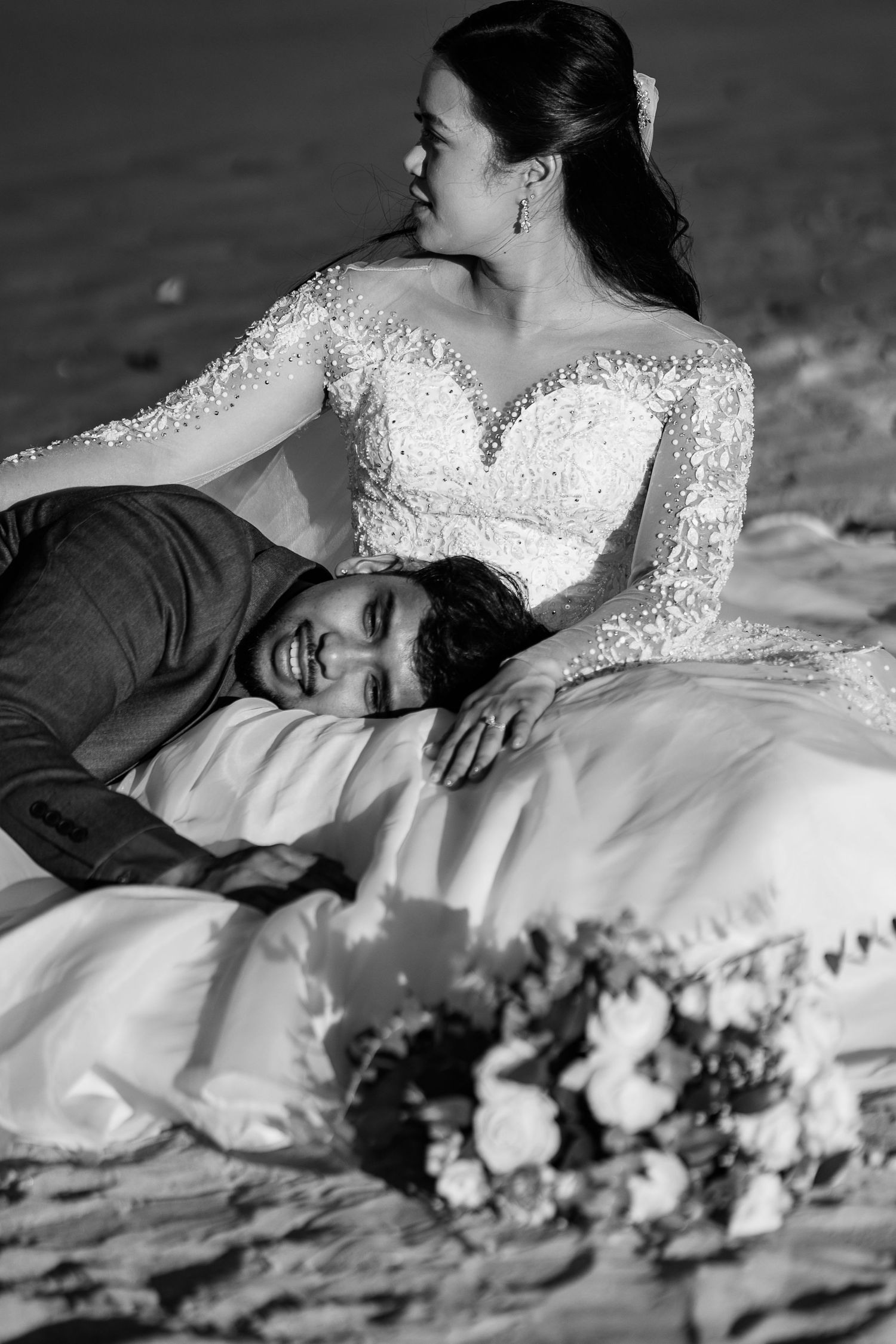 Intimate black and white portrait of couple in wedding attire laying together.