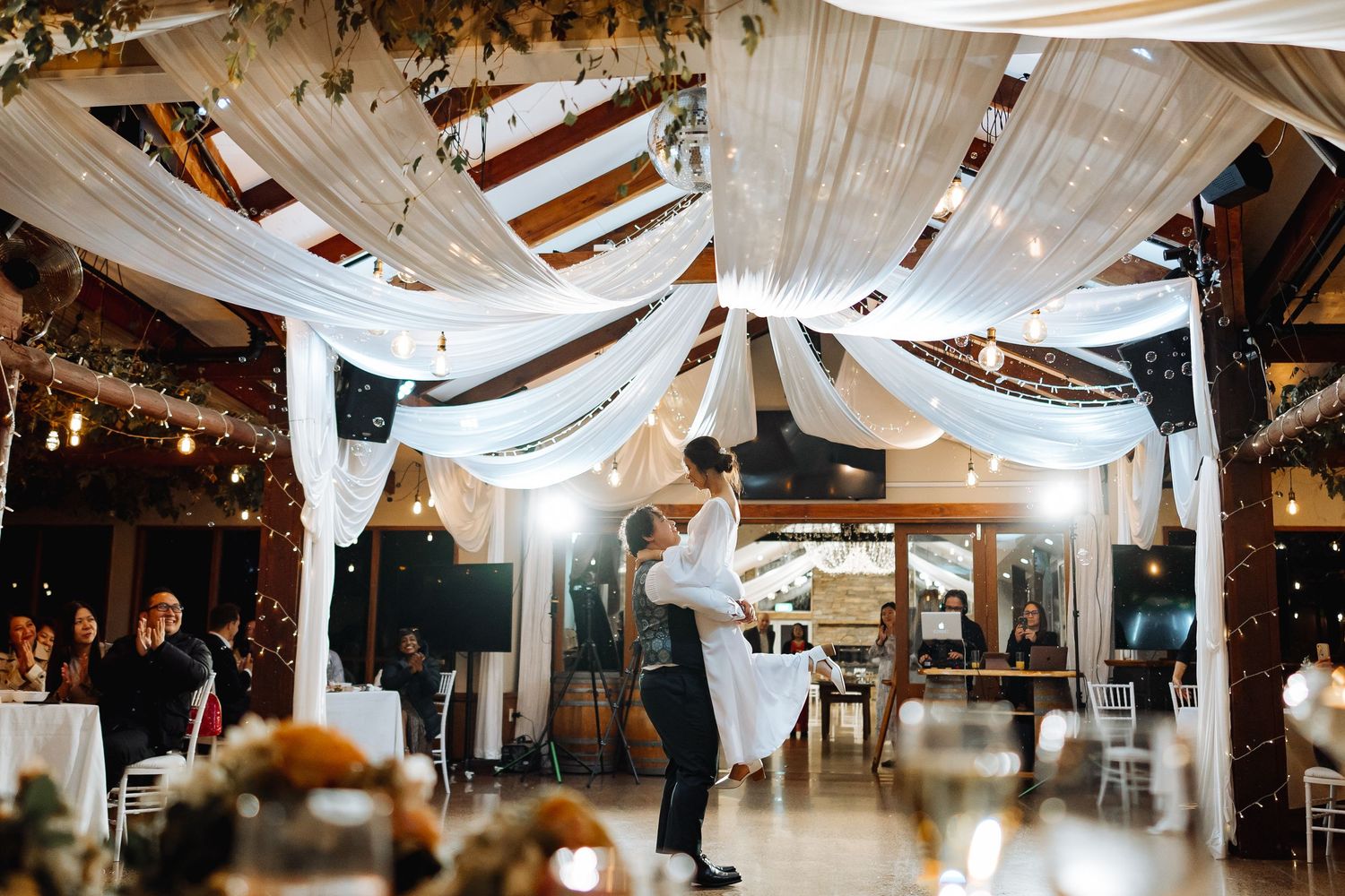 Indoor wedding reception space with white fabric ceiling drapes and warm lighting.