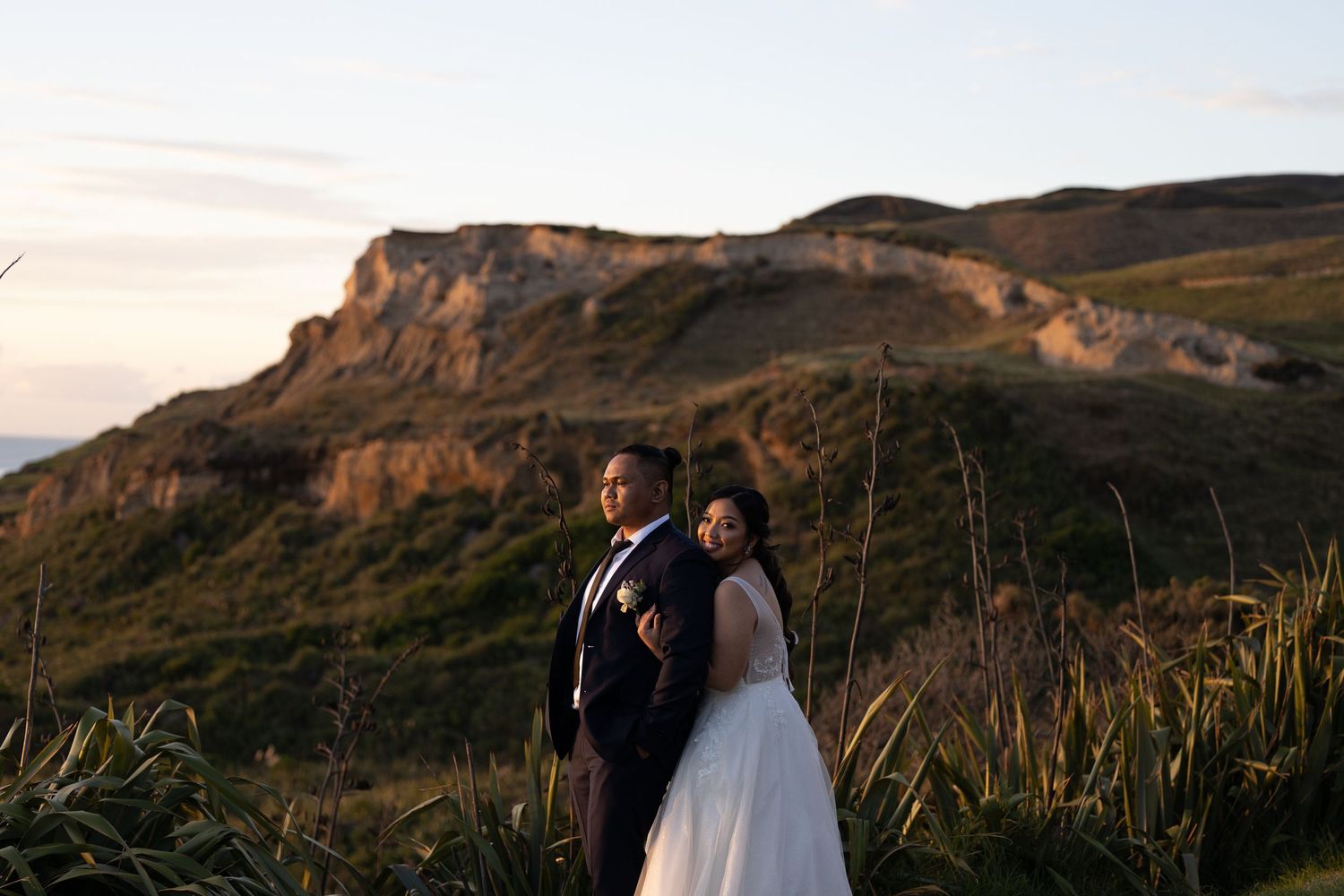 Couple poses for romantic sunset photos against dramatic mountainous coastal landscape.
