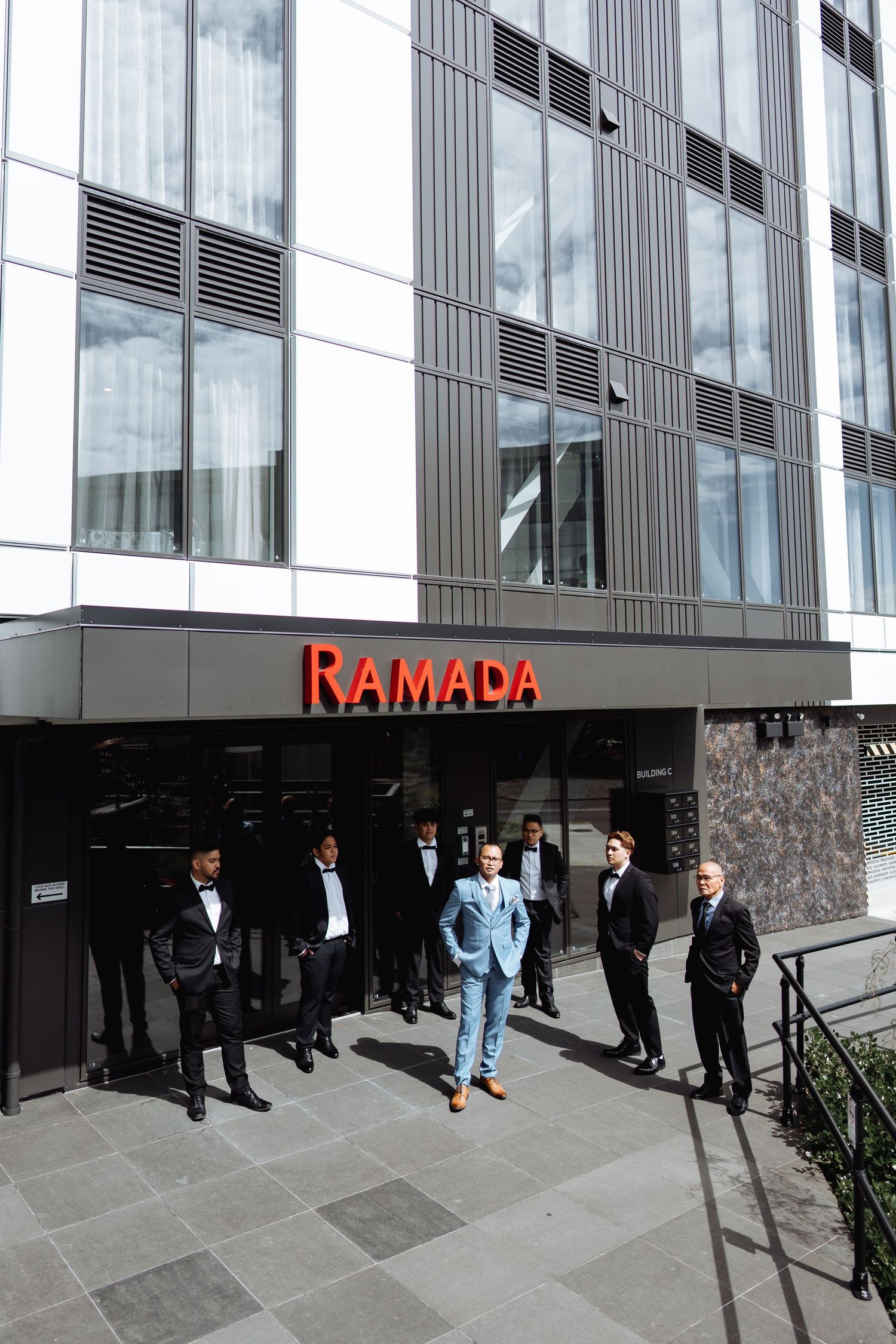 Wedding party members gather outside a modern building with Namada signage.