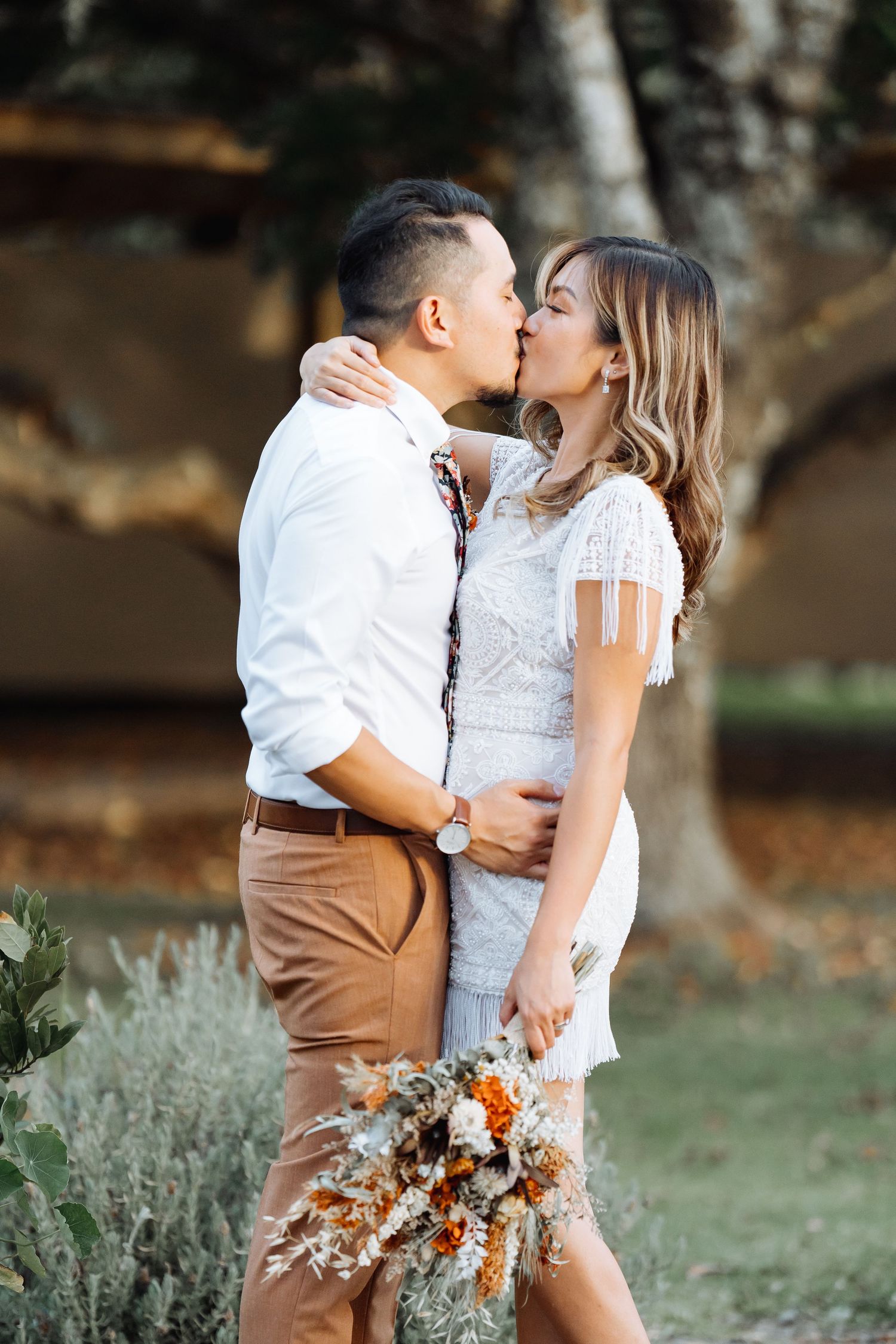 A romantic outdoor engagement photoshoot featuring a couple in white and brown outfits with a fall-themed bouquet.