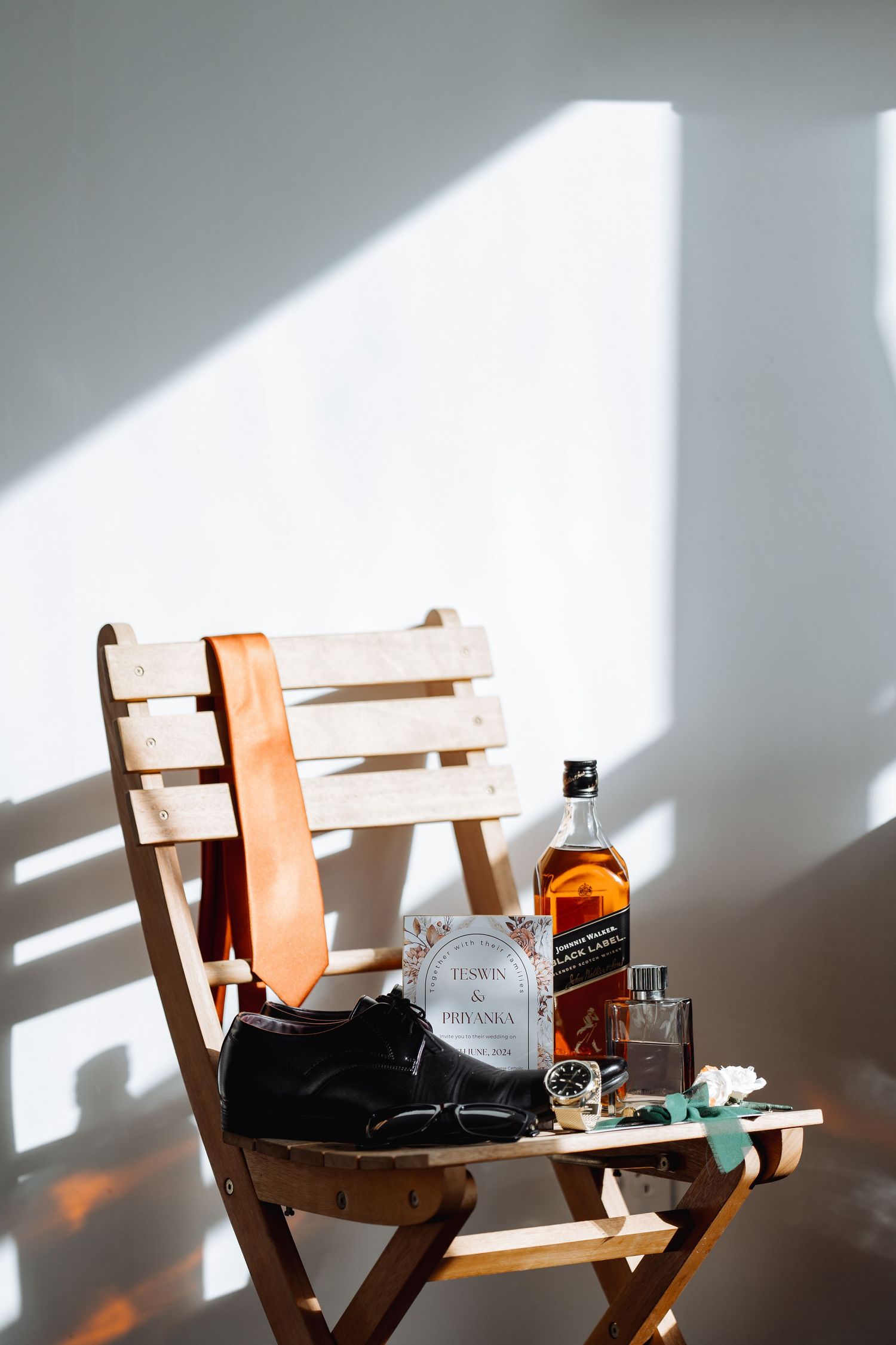 Whiskey bottles and wedding accessories arranged on wooden chairs with dramatic window lighting.