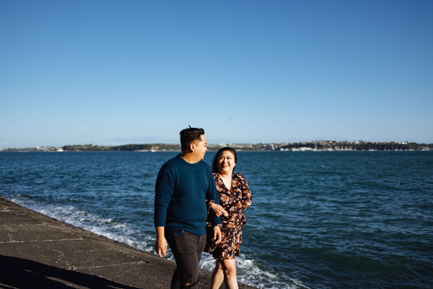 A couple walks along the waterfront with ocean views and blue skies.