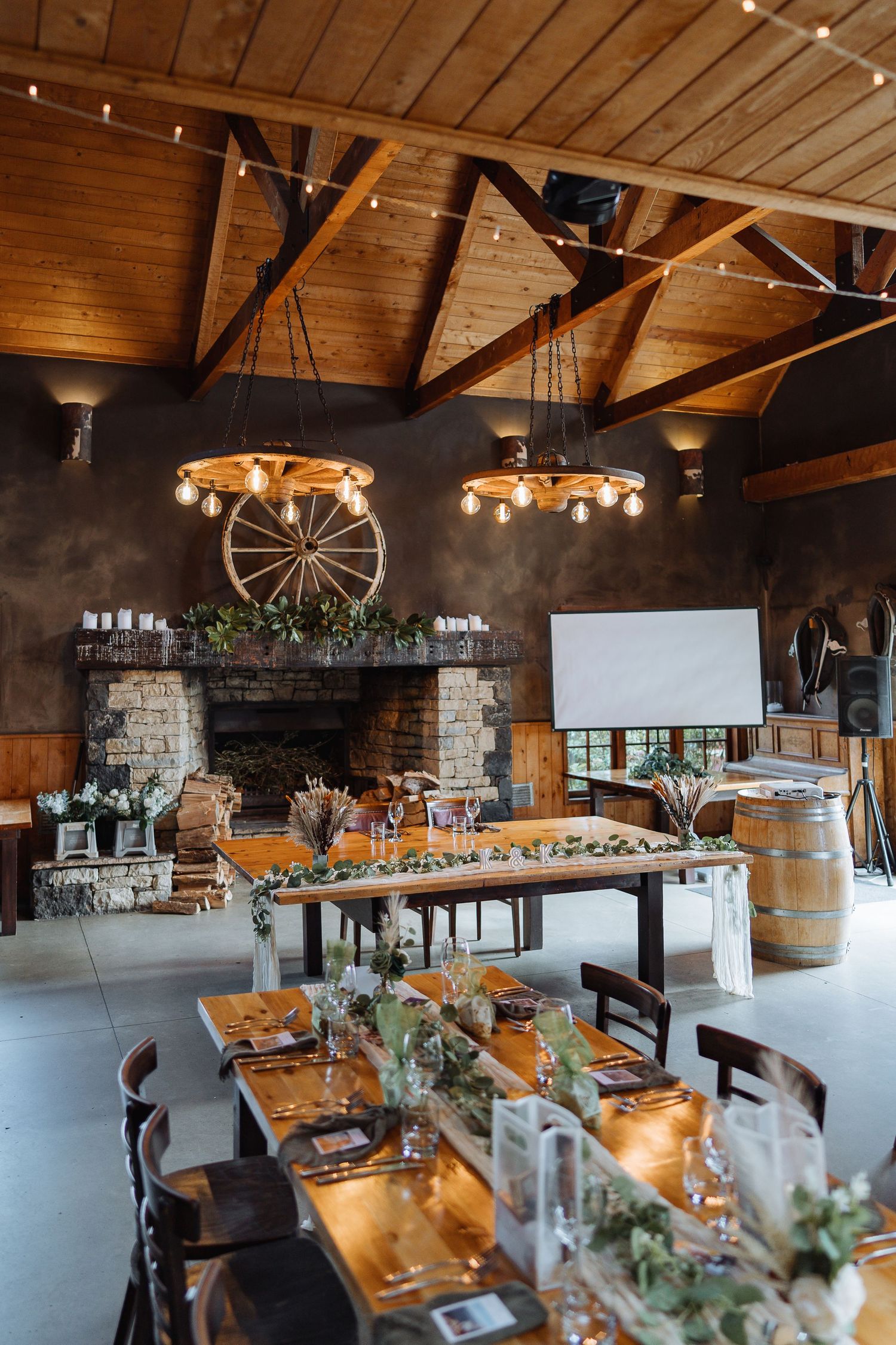 Rustic barn venue interior with exposed wooden beams, string lights, and elegant table settings for a wedding reception.
