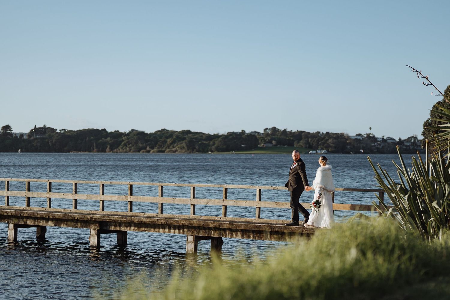 Long wooden pier stretches across calm water under blue sky.