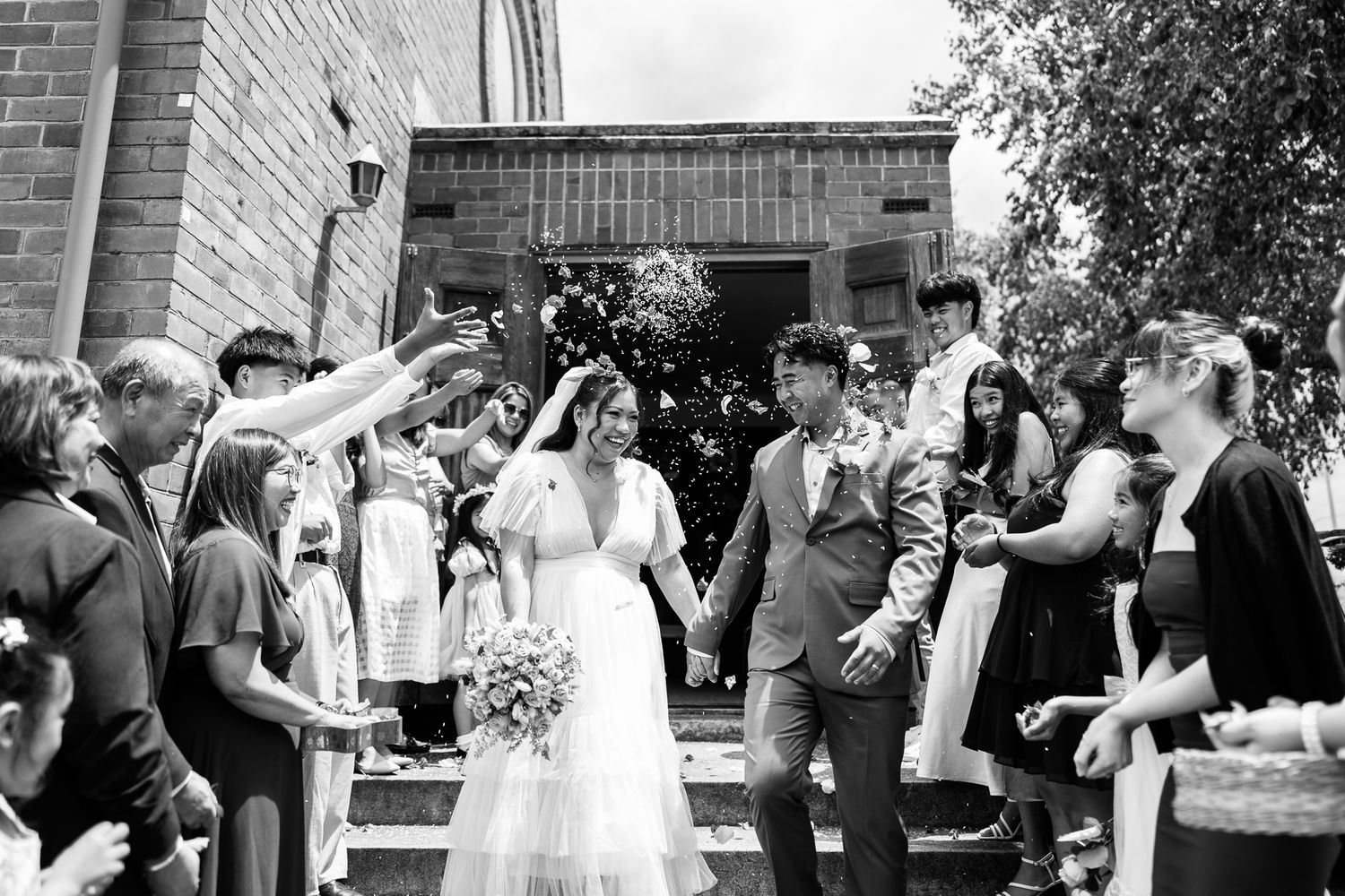 Wedding celebration exit with guests throwing confetti outside brick church.